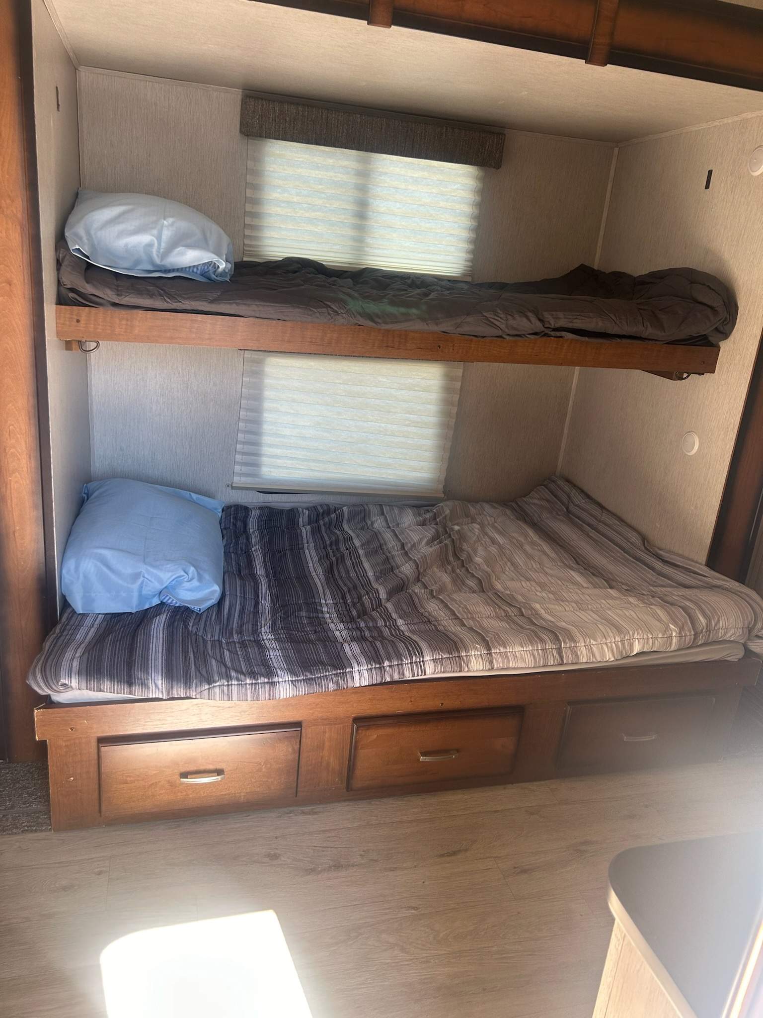 Inside an RV rental: cozy stacked bunk beds with bedding, pillows, windows, and convenient under-bed storage.. Heartland RVs Pioneer 2019