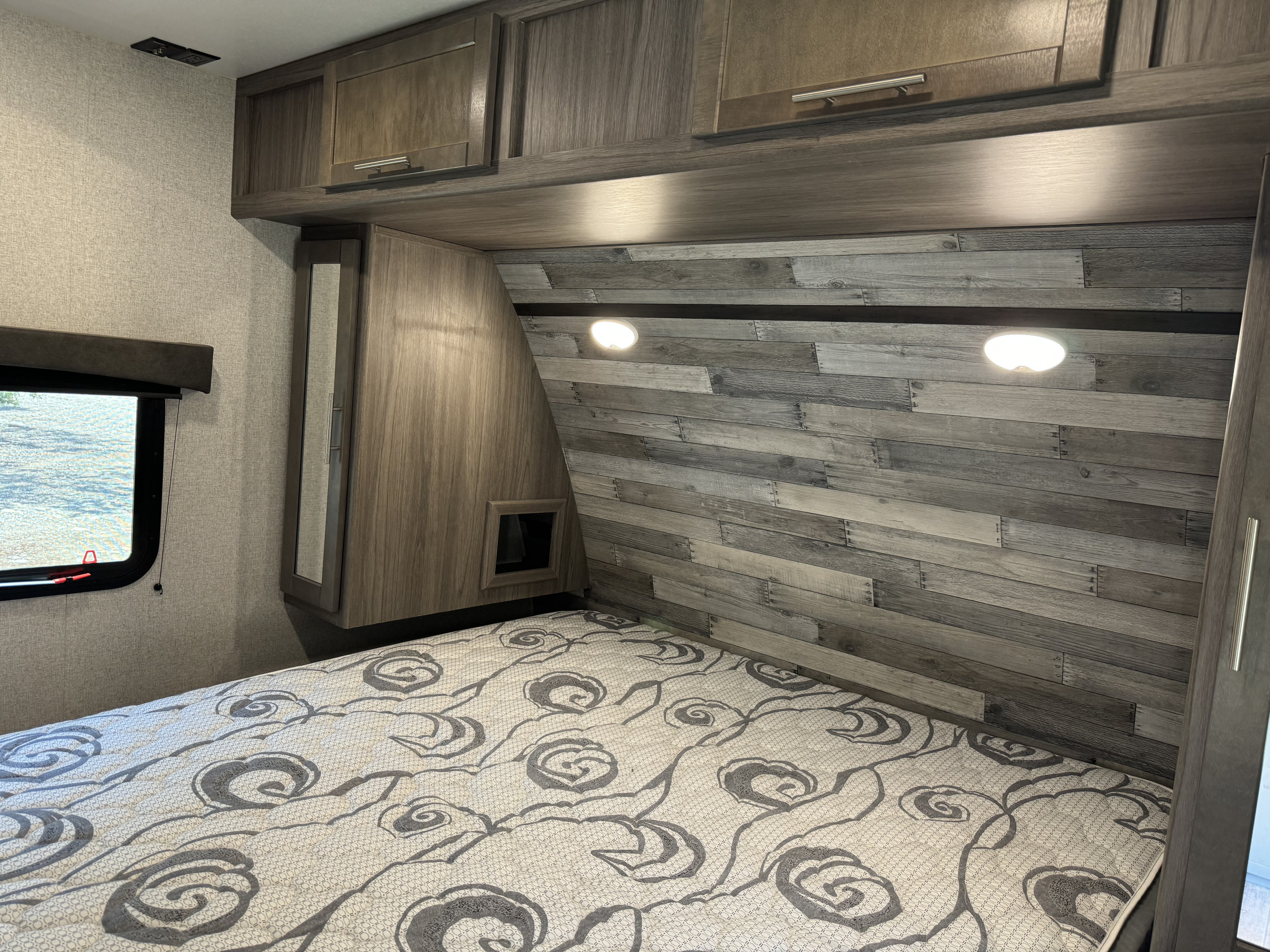 Modern RV rental bedroom featuring a comfortable bed, wood paneling, and storage. Ideal for cozy travels.. Crossroads RV Volante 2020