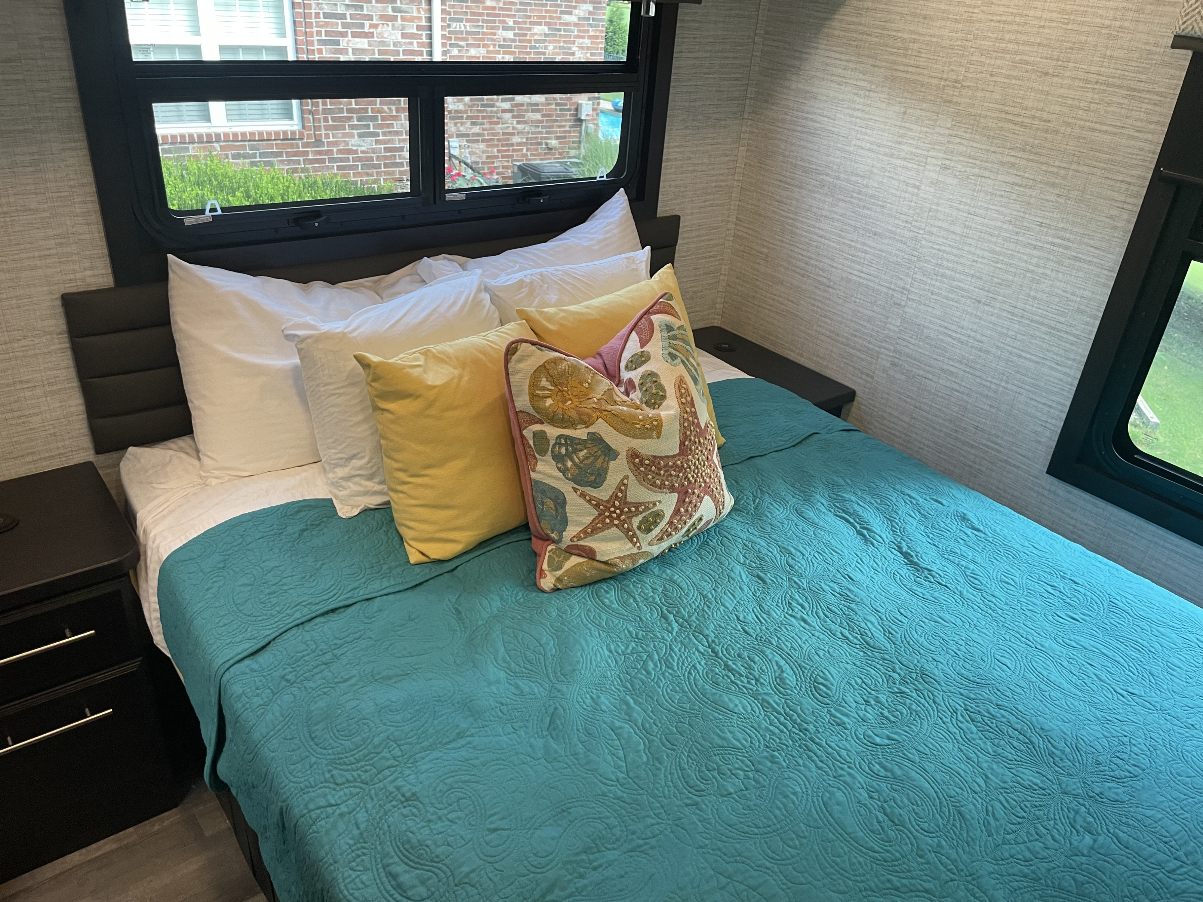 Cozy RV rental bedroom with a teal quilt, plush pillows, and windows offering a view outside.. Jayco Greyhawk 2024