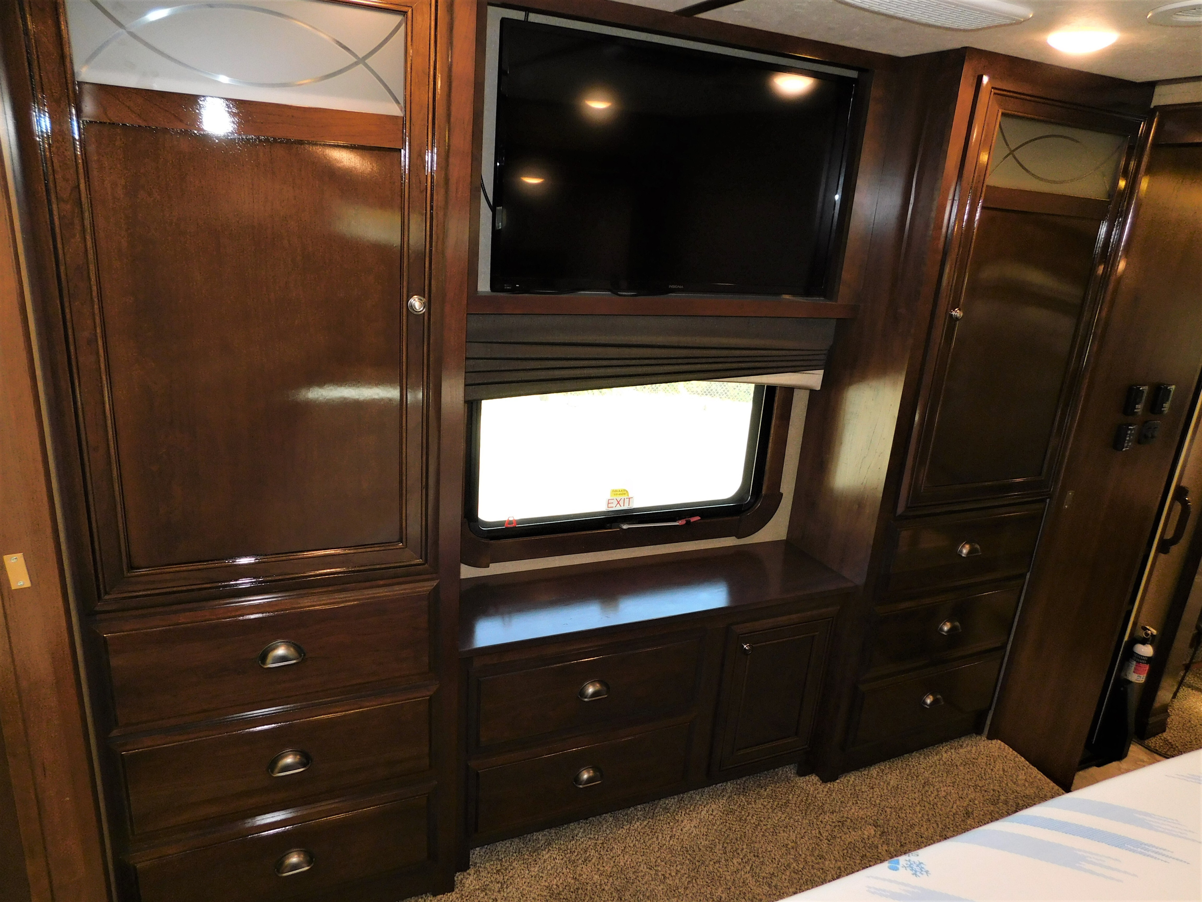 Spacious RV rental bedroom with dark wood built-in storage: TV, cabinets, drawers, and an emergency exit window.. Thor Motor Coach Redwood 2019