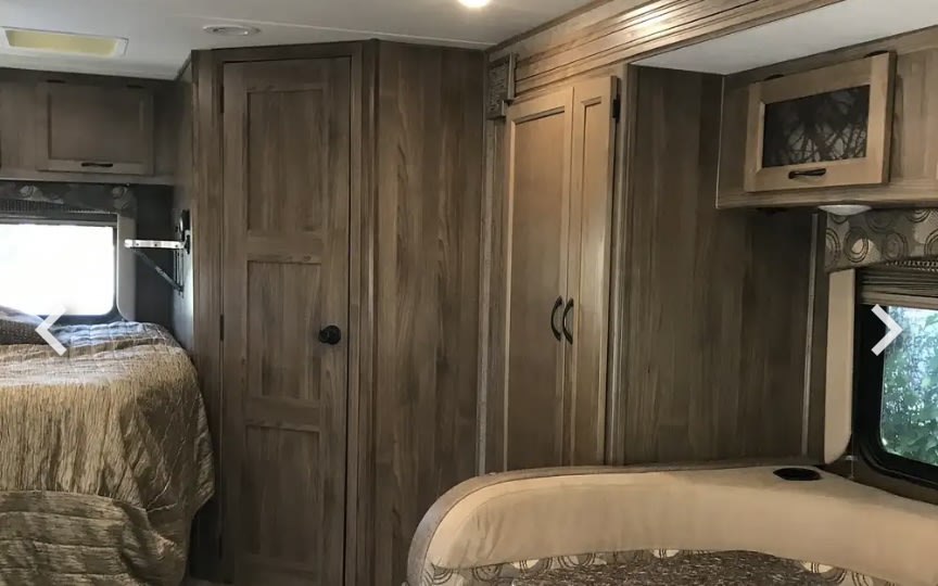 Spacious RV rental bedroom with a comfy bed, window, and ample wood storage cabinets.. Forest River Coachmen Freelander 2017