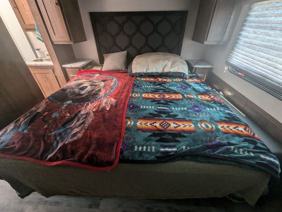 Compact RV rental bedroom featuring a bed with two patterned blankets, built-in storage, and a window.. Coachmen Pursuit 2021