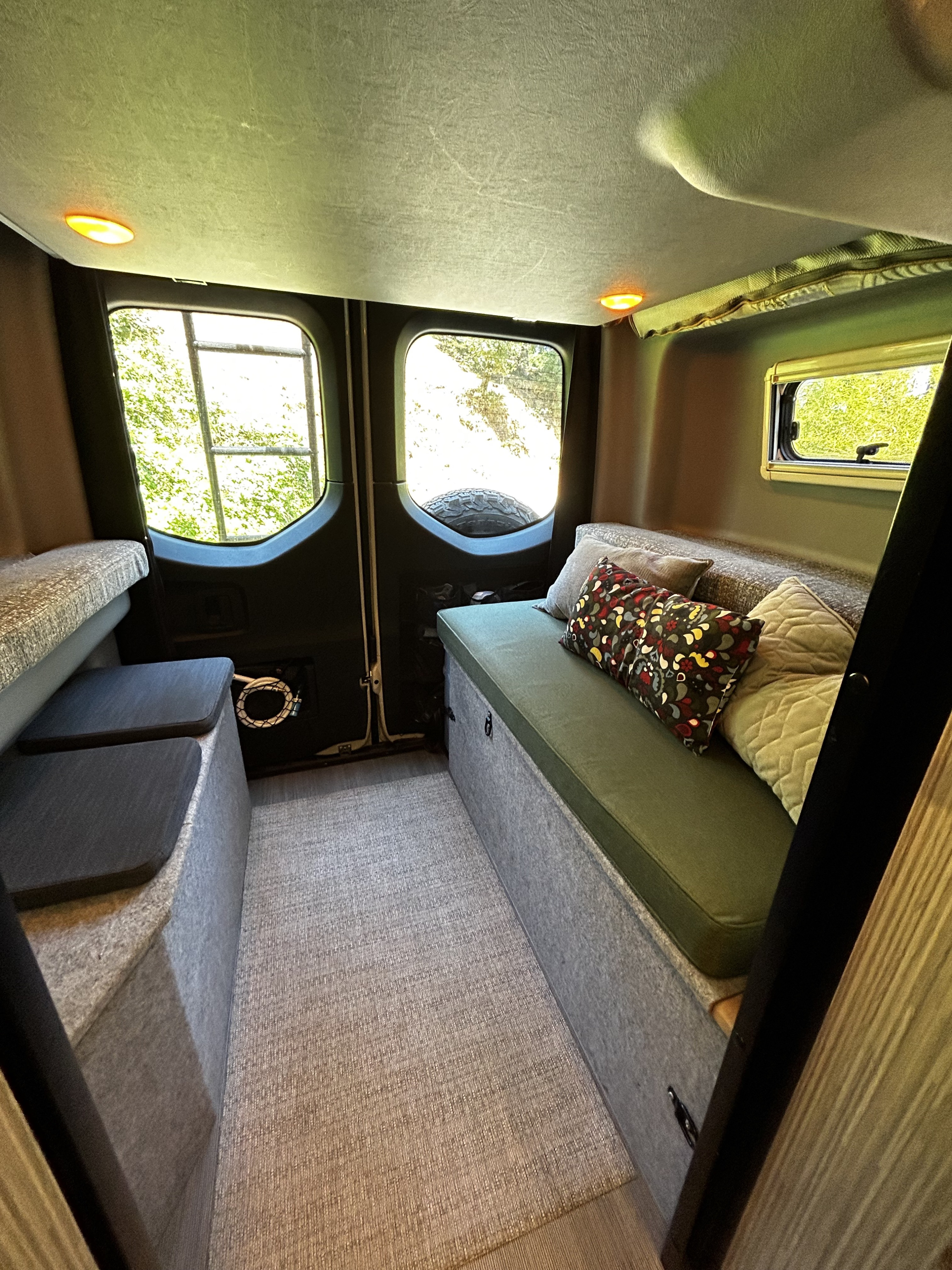 Cozy RV rental interior: bench seating, cushions, windows with views, and warm overhead lighting.. Winnebago Revel 2020