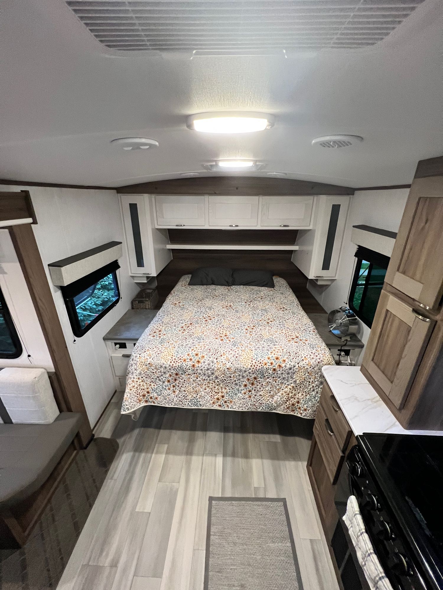 Cozy RV rental interior showing bedroom, living area, and kitchen. Features light wood flooring and floral quilt.. Heartland RVs 1900RB MPG 2023