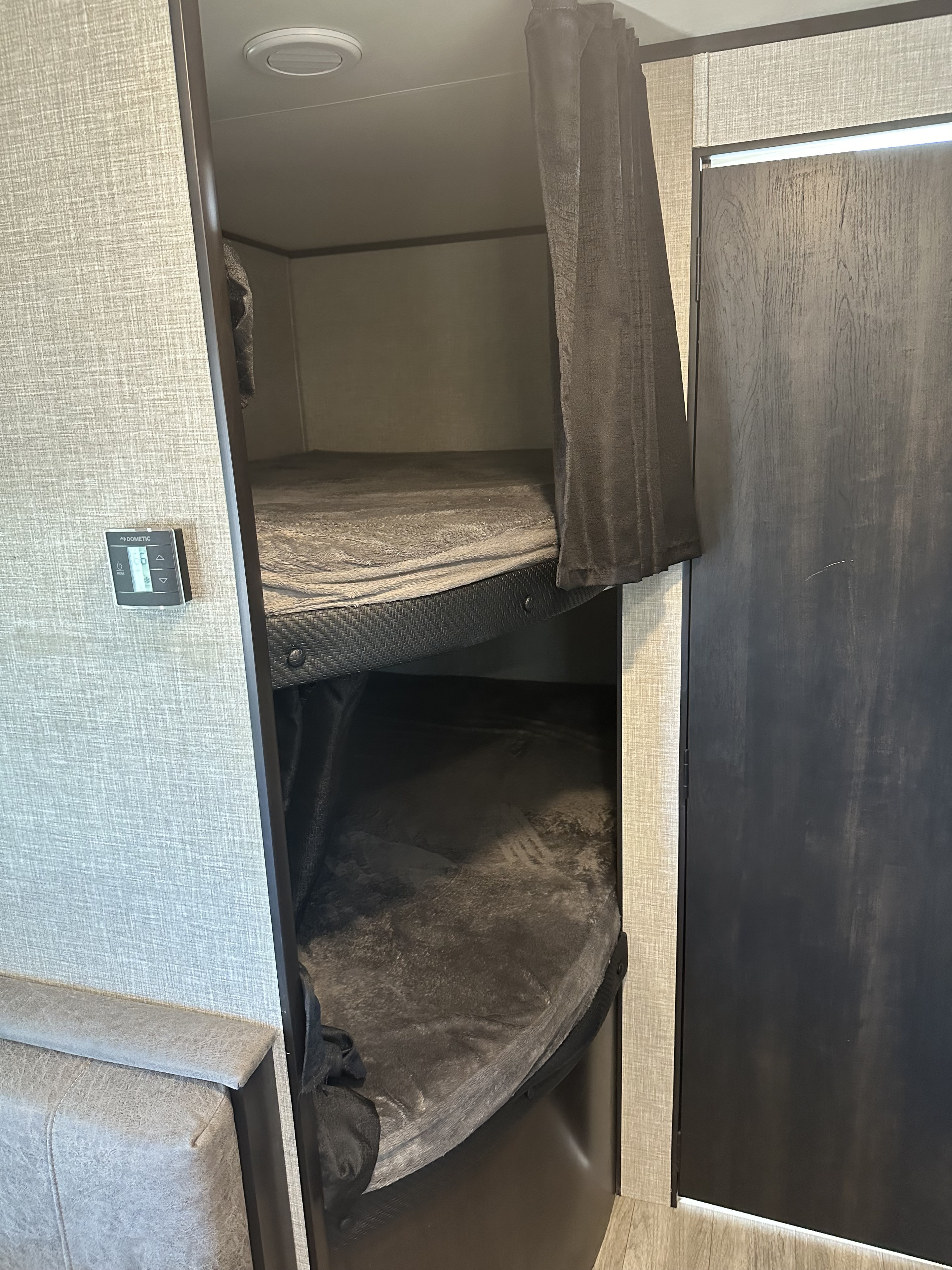 RV rental interior showcasing two cozy bunk beds with dark bedding, a privacy curtain, and a Dometic control panel.. Jayco Jay Flight 2022