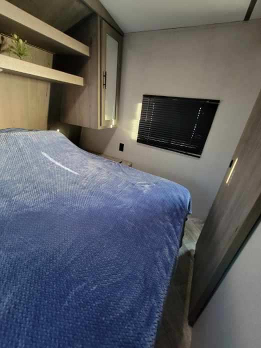 Inside an RV rental: a compact bedroom featuring a bed with blue comforter, built-in shelving, and a window.. Keystone RV Springdale 2021