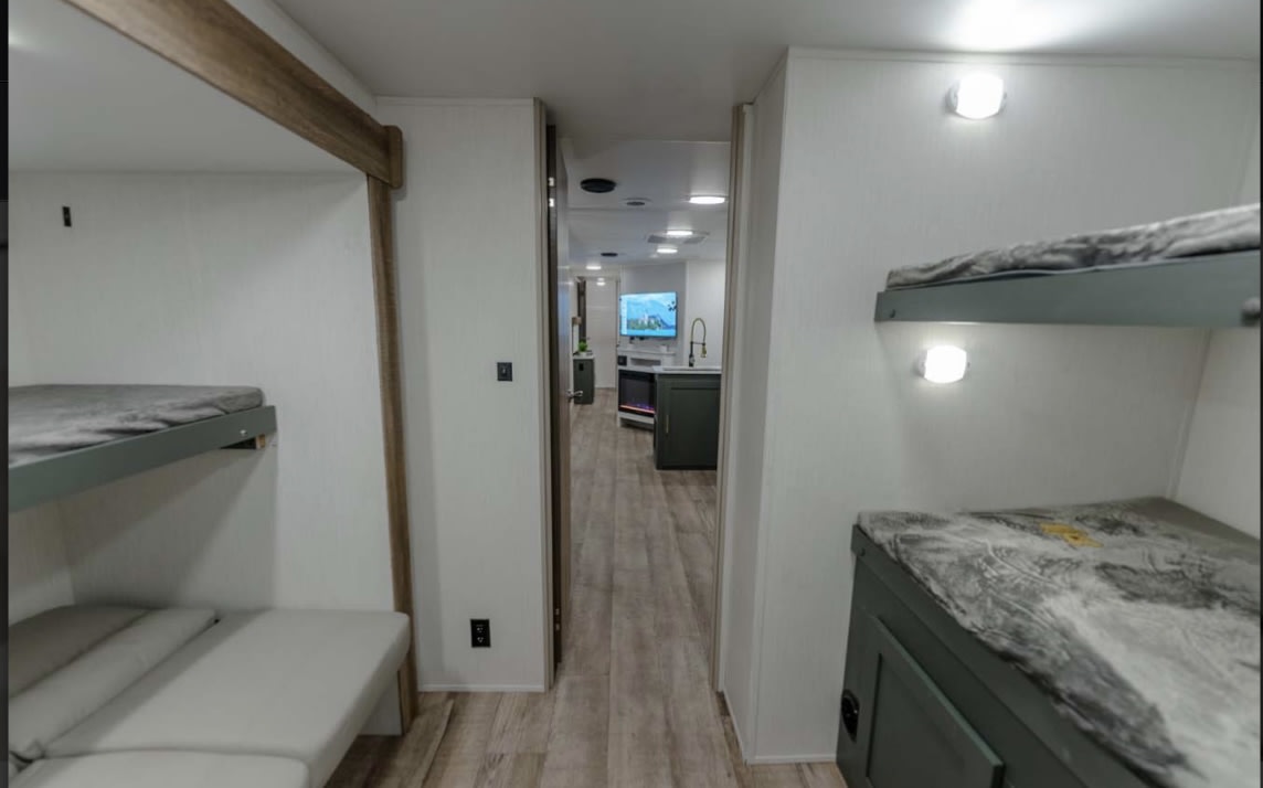 Inside a bright RV rental: bunk beds on both sides, with a clear view into the main living & kitchen area.. Heartland RVs Eddie Bauer BHS 34 2024