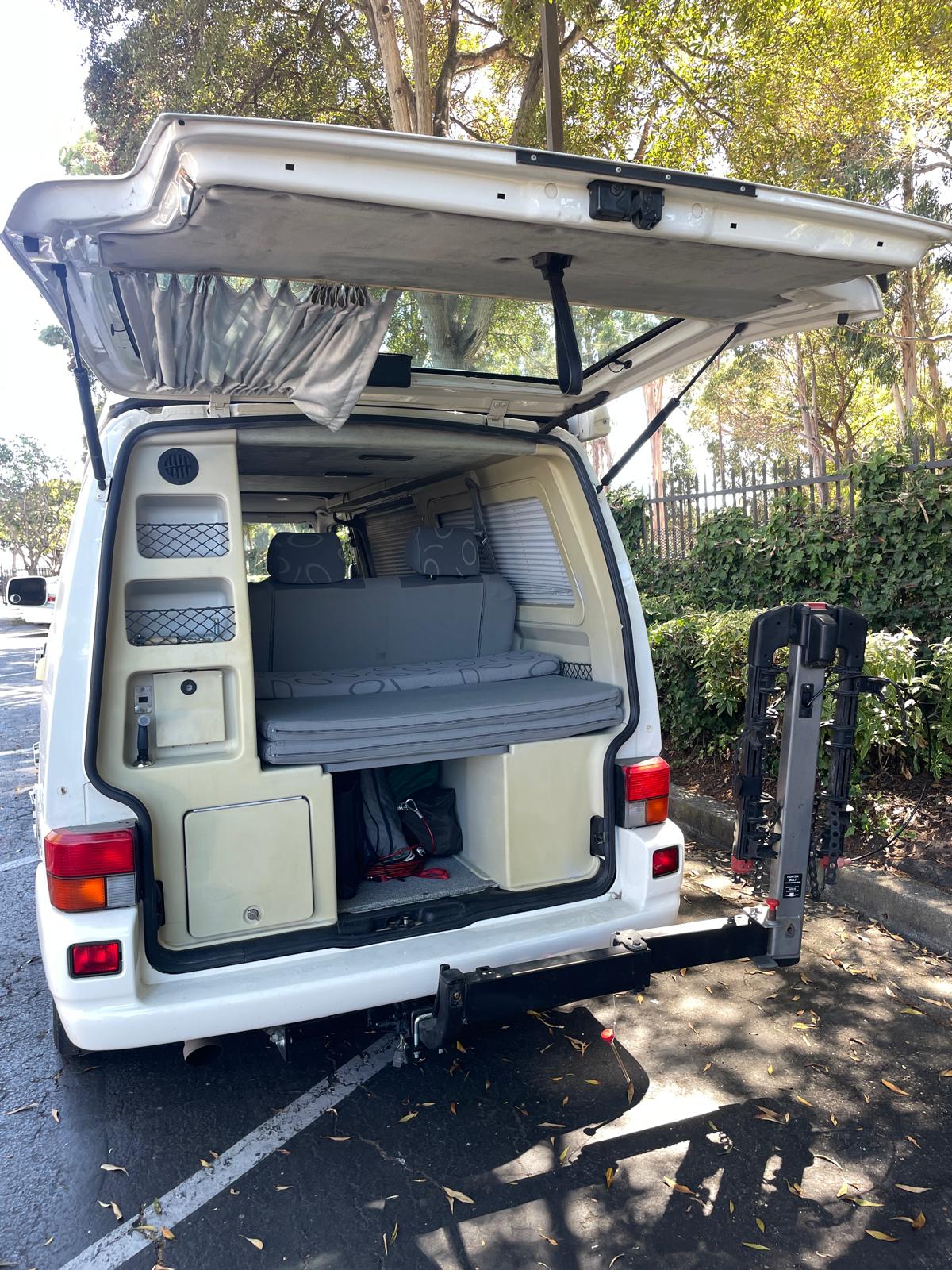 An **RV rental** camper van with its tailgate open, revealing a convertible bed, built-in storage, and a rear bike rack.. Volkswagen Eurovan 1999