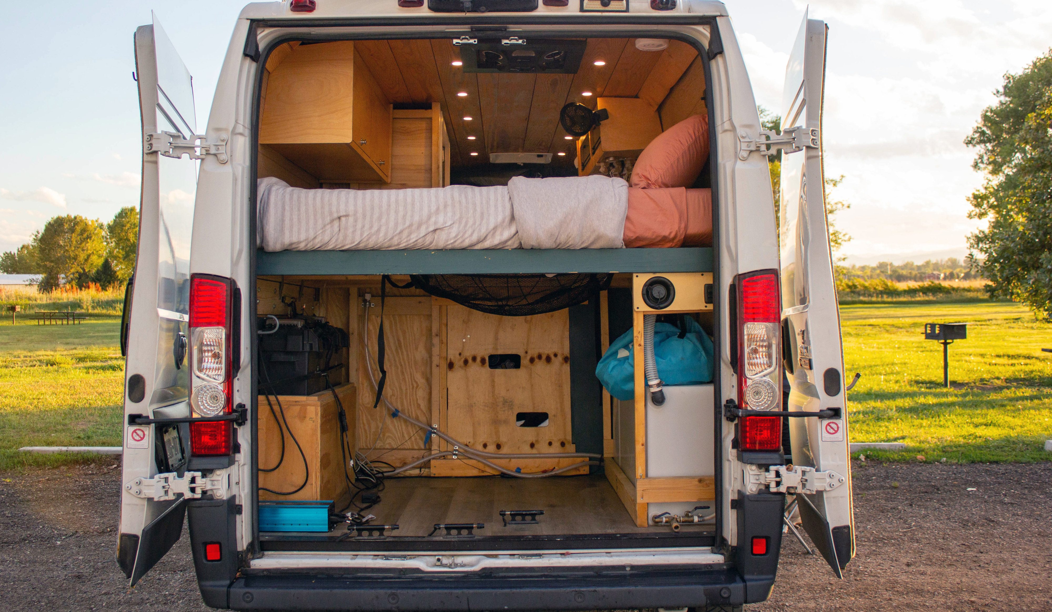 Custom camper van, perfect for an RV rental adventure, reveals its cozy bed, ample storage, and utility setup through open rear doors.. Dodge Promaster 2500 2016