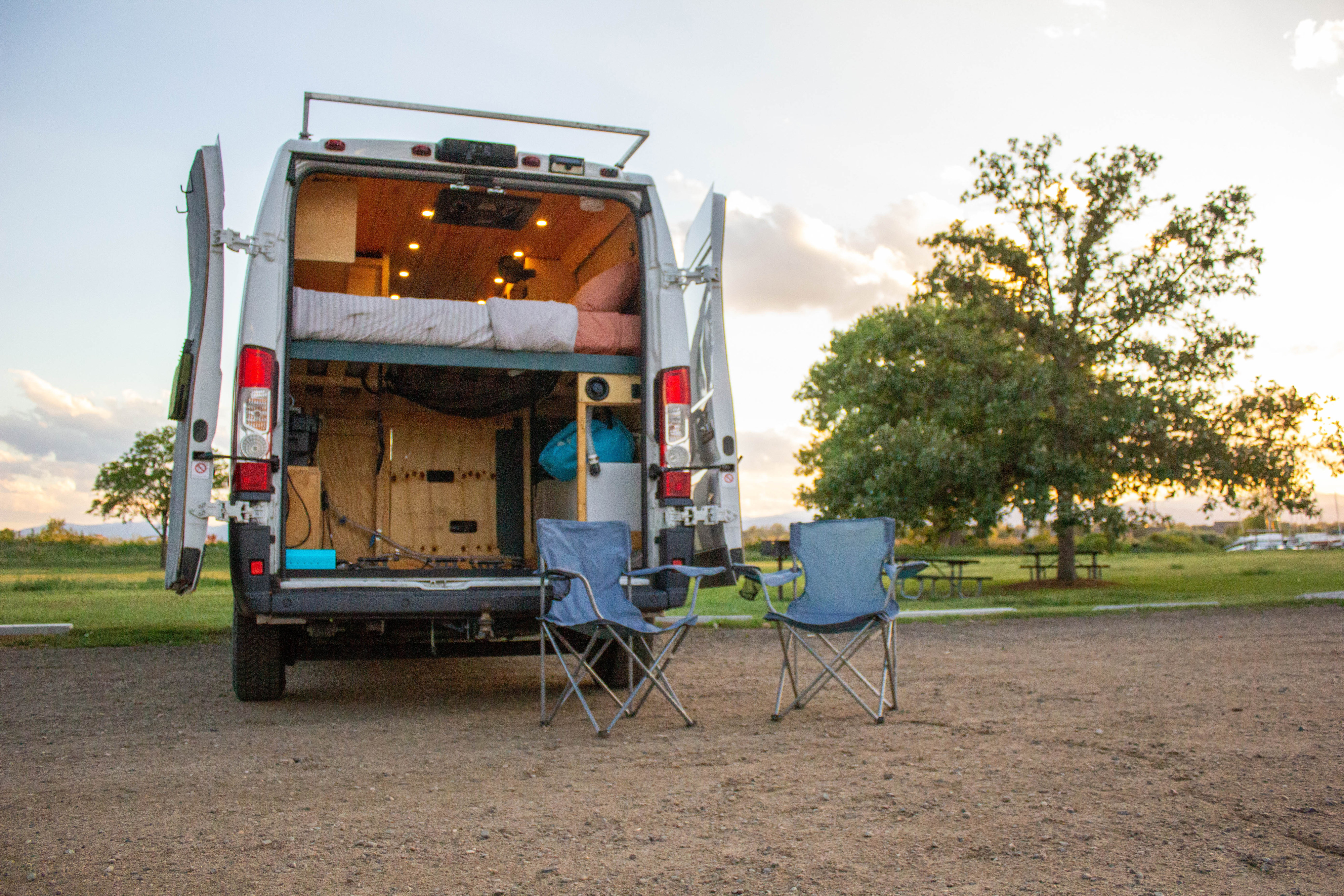 Cozy RV rental camper van with open back, revealing bed inside; two chairs are set out for camping relaxation.. Dodge Promaster 2500 2016