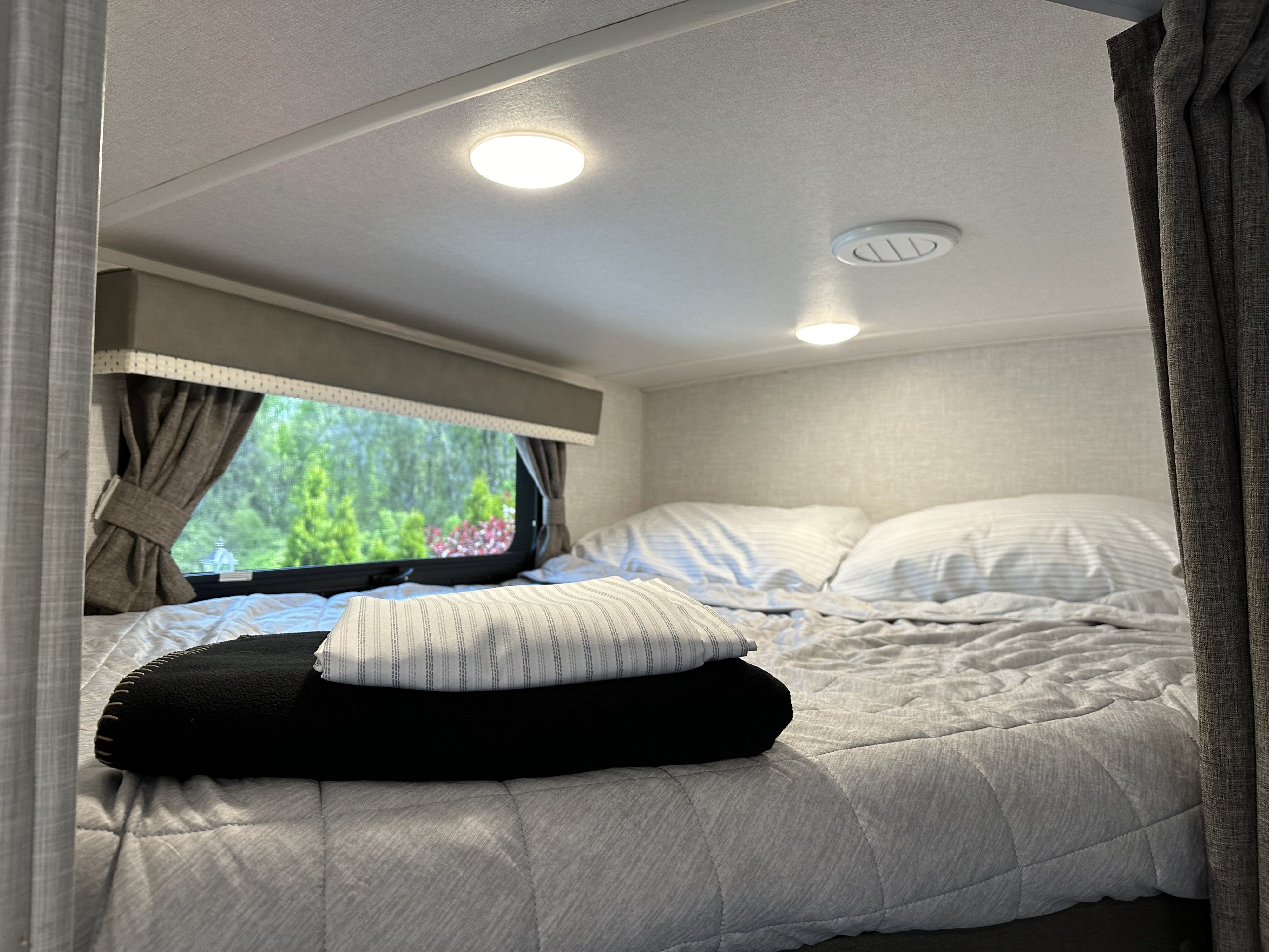 Cozy RV rental bedroom with a comfy bed, striped linens, and a scenic window view of nature.. Forest River Rockwood Mini Lite 2022