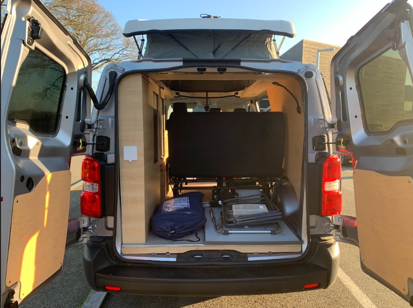 Explore this versatile RV rental: customized camper van interior with pop-top roof and visible camping gear.. Peugeot e-expert 2022