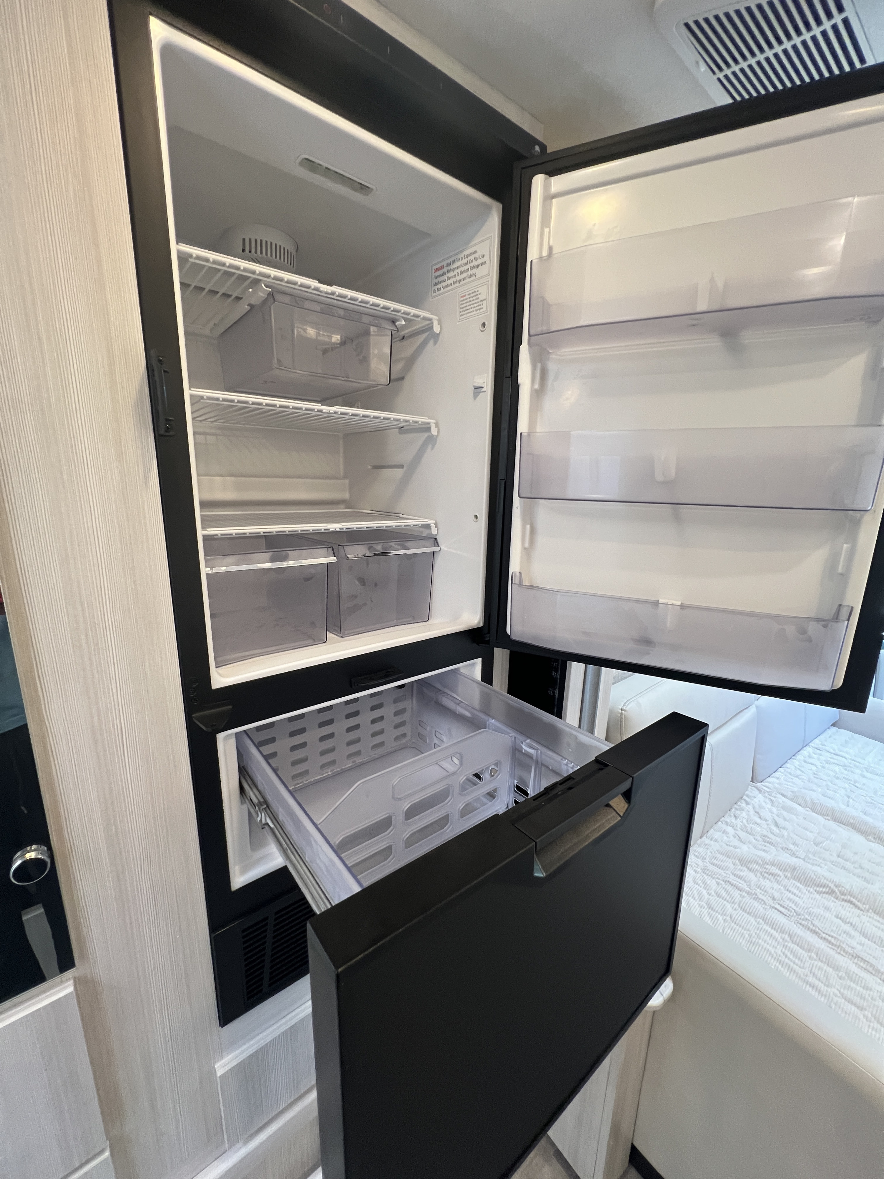 Open compact RV rental fridge and freezer drawer showing interior storage, shelves, and bins.. Thor Compass 2024