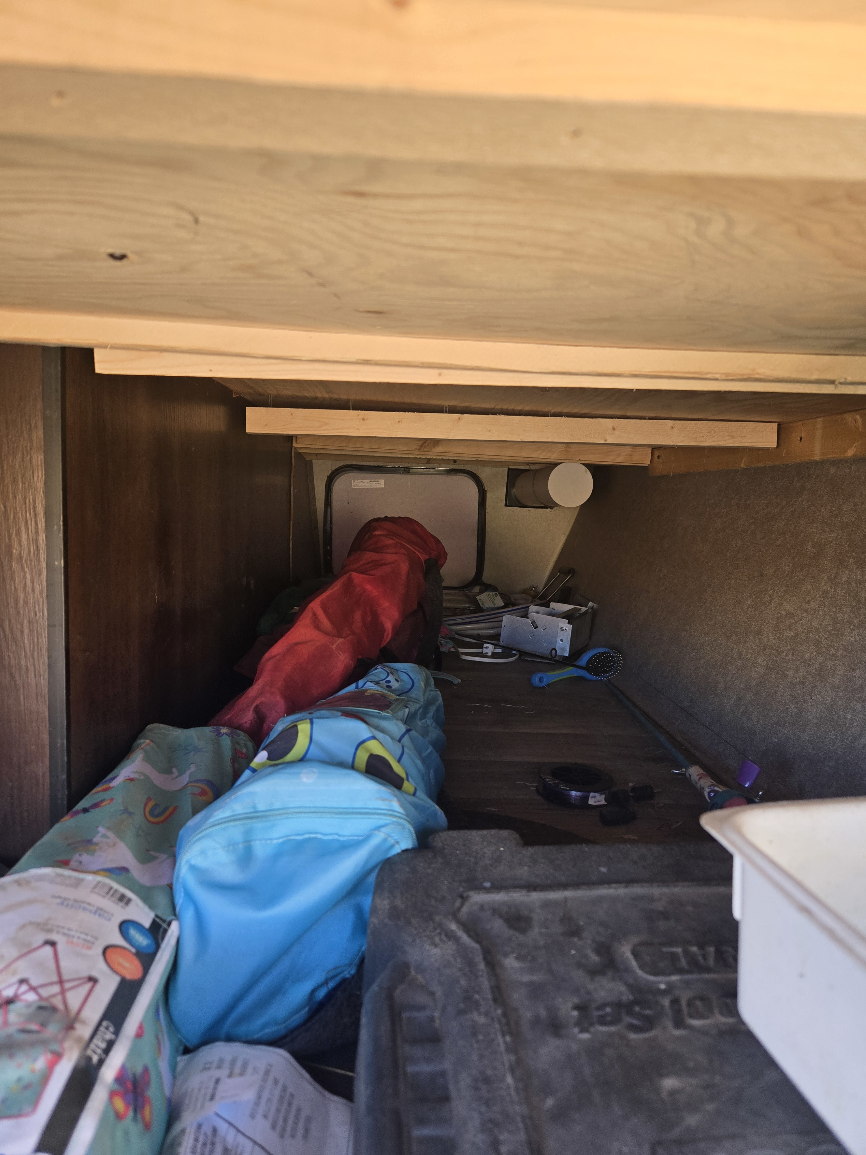 Inside a cluttered RV rental storage compartment, various camping gear, bags, and a fishing rod are visible.. Jayco Octane 2018