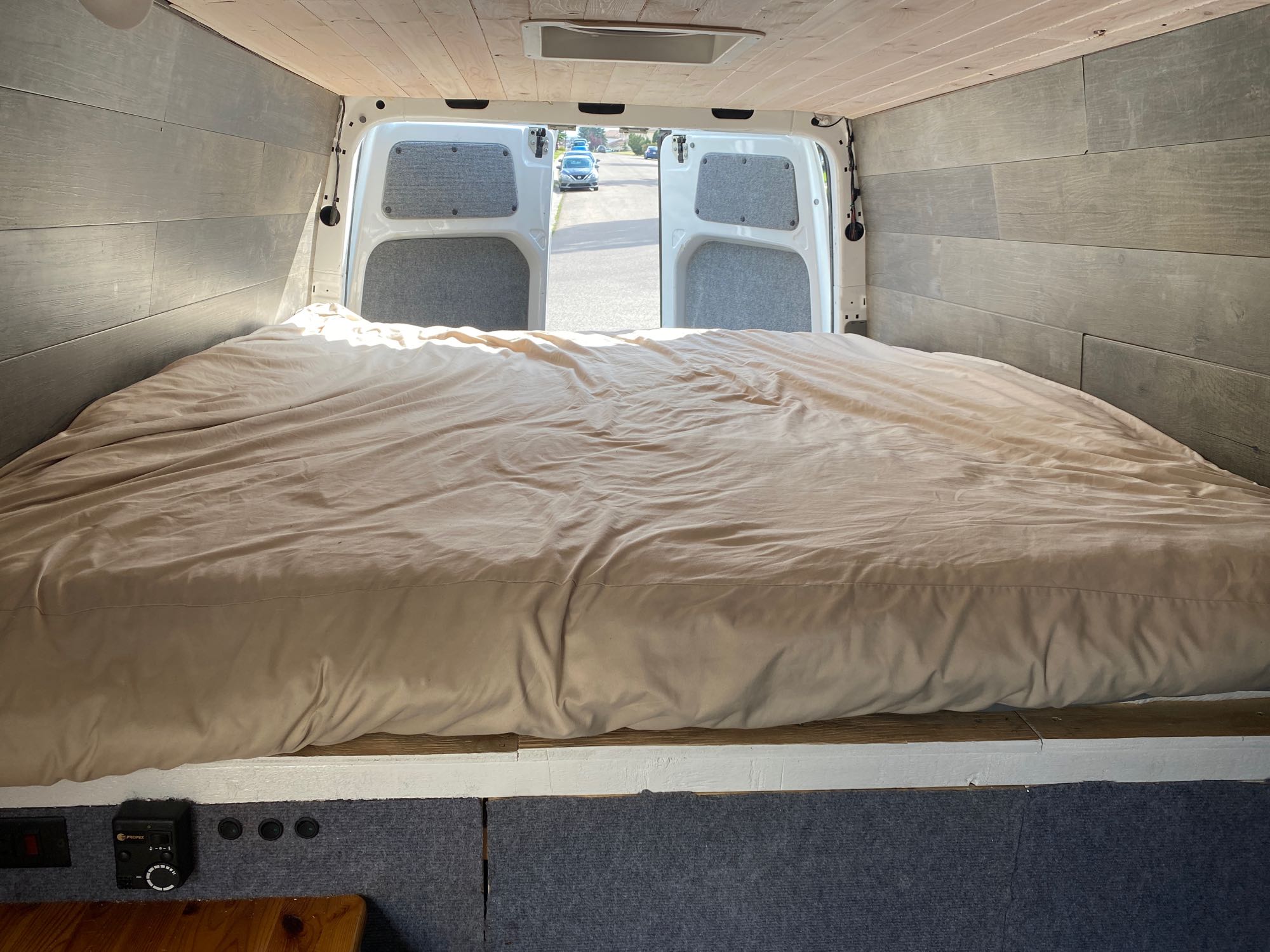 Cozy RV rental interior shows a large bed, gray plank walls, and open rear doors looking out to a residential street.. Mercedes-Benz Sprinter 2013