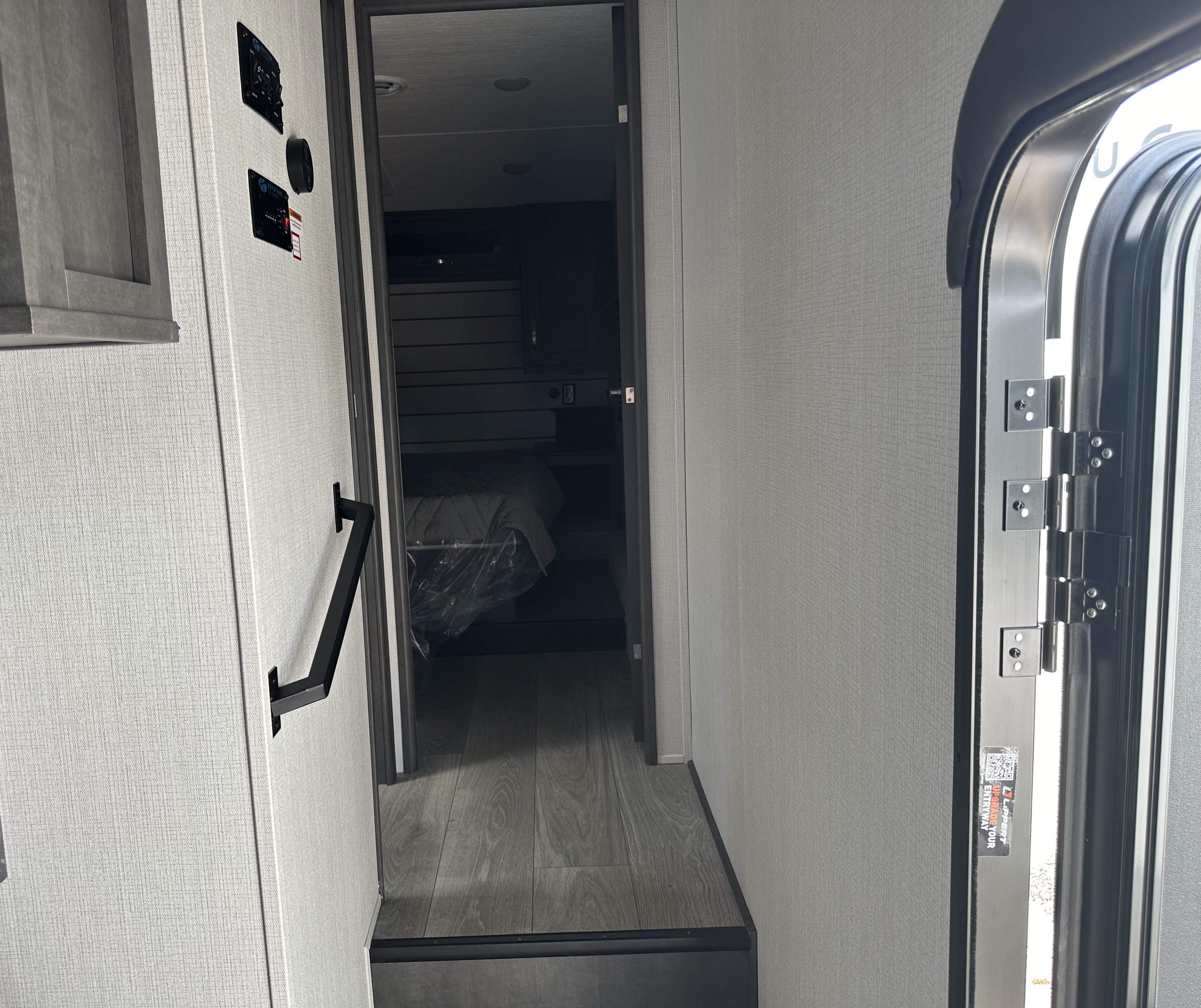 RV rental interior showing an entryway, wall controls, grab handle, and a dark bedroom with a bed.. Keystone Cougar Sport 2700BH 2024