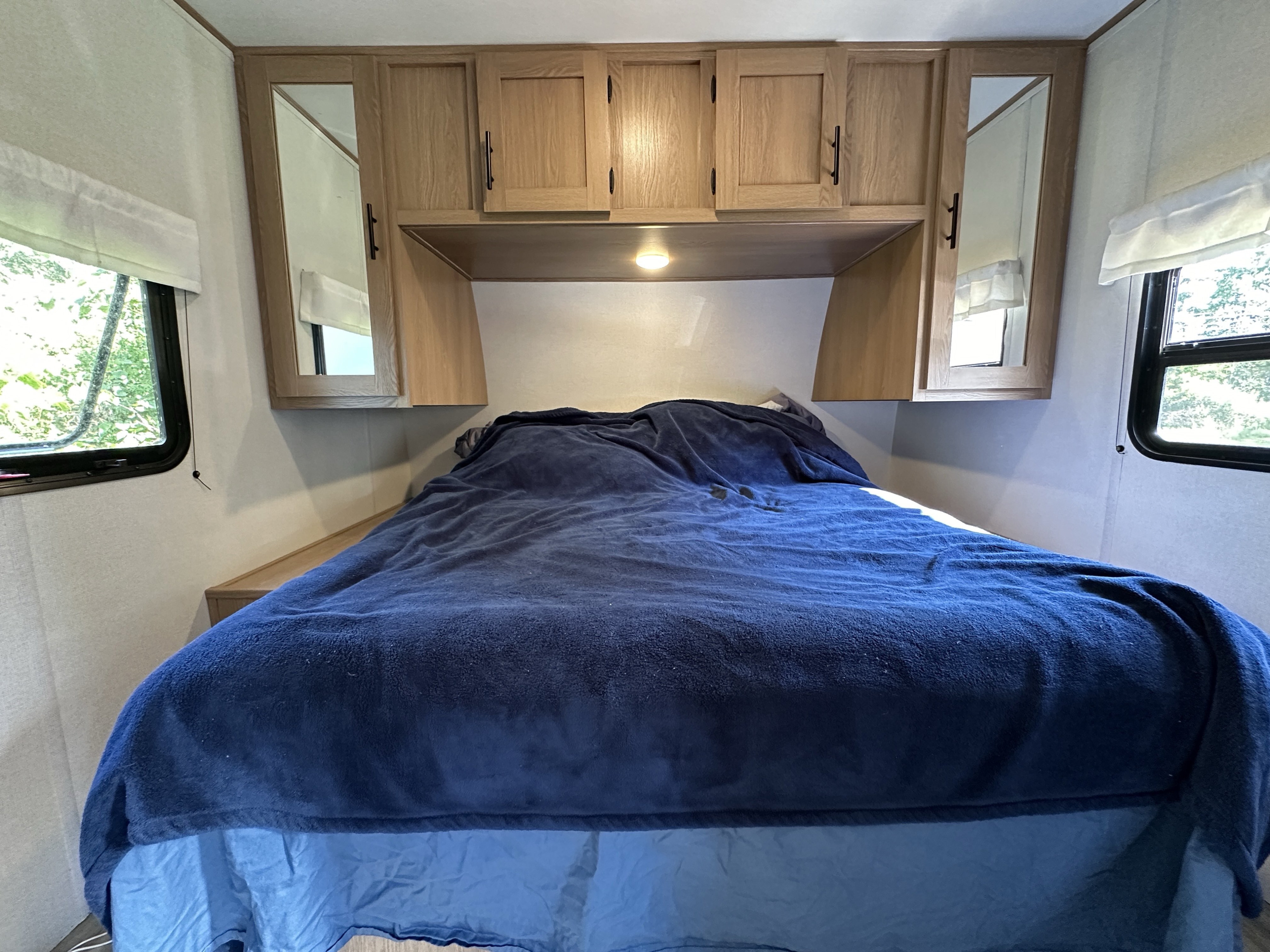 Inside an RV rental: a neat bedroom with overhead cabinets, mirrored wardrobes, and a cozy blue-covered bed.. Avenger Avenger Trailer 2022