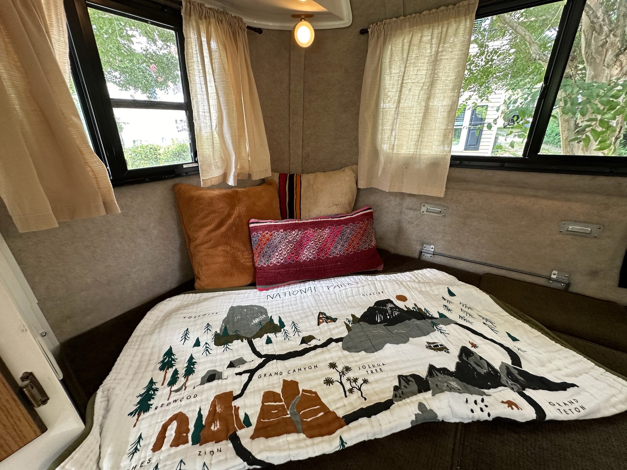Cozy RV rental interior featuring a National Parks map blanket, plush pillows, and bright windows with views of trees.. Scamp Scamp Trailer 2011