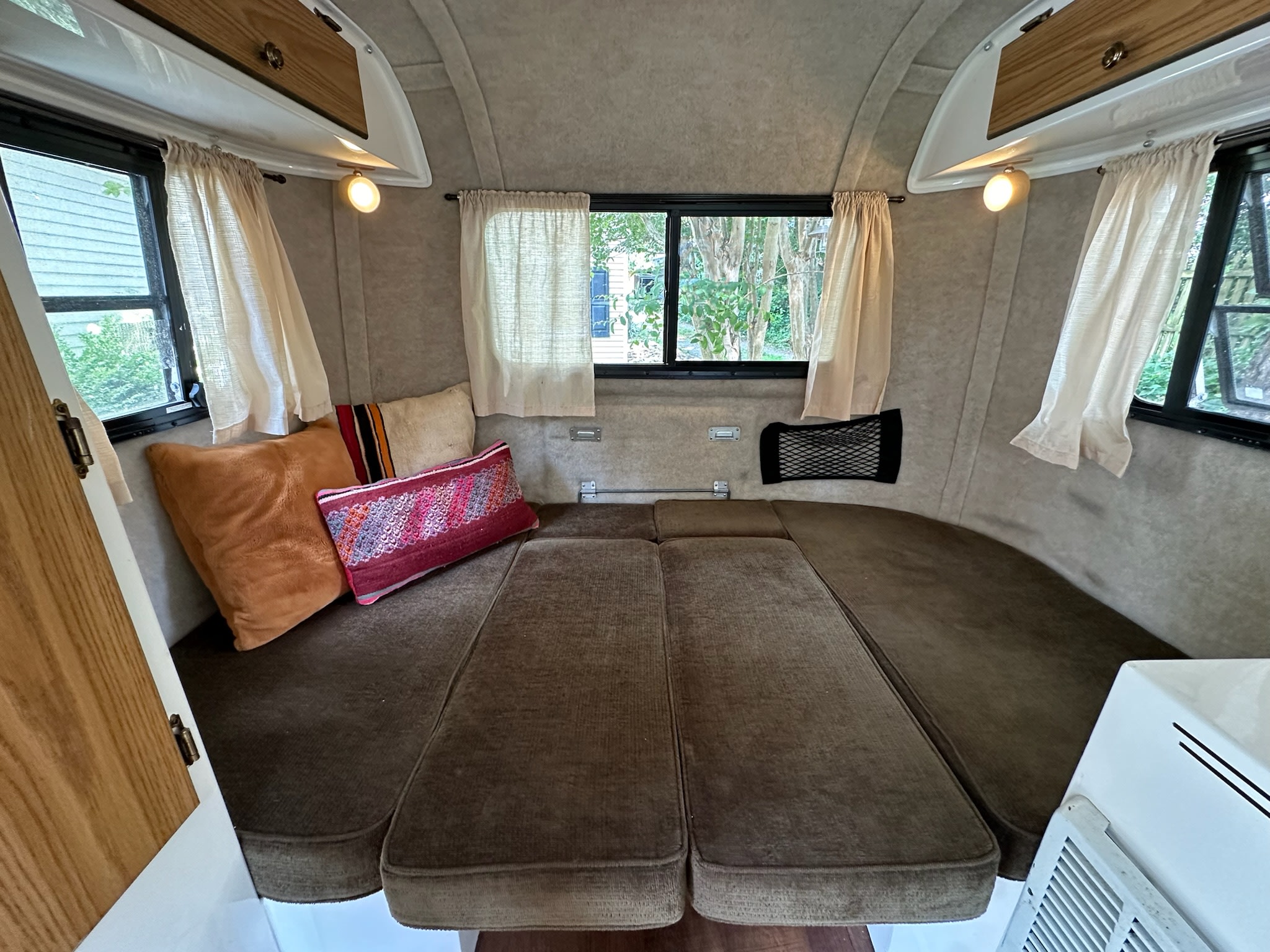 This RV rental shows a compact interior with a brown cushioned bed, windows with curtains, and overhead storage.. Scamp Scamp Trailer 2011