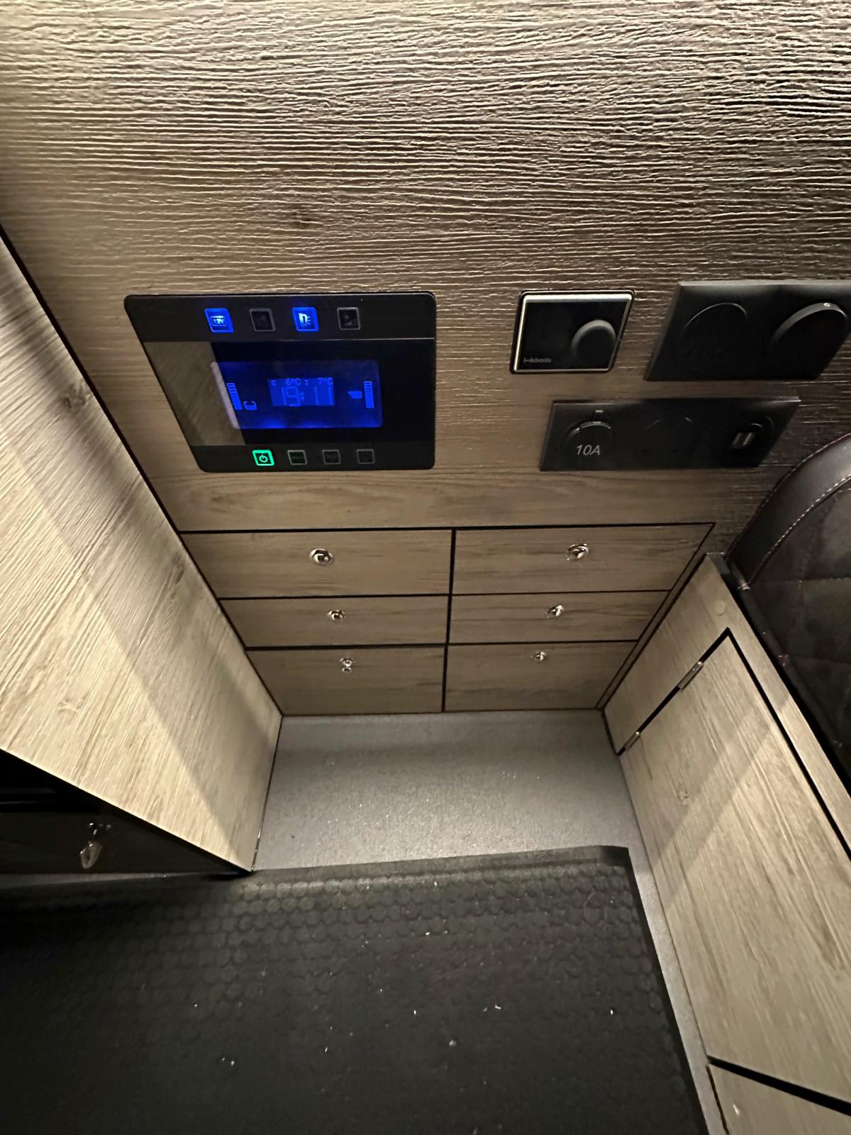 RV rental interior showcasing a digital control panel with blue display, heating controls, power outlets, and light wood drawers.. Renault Other 2023