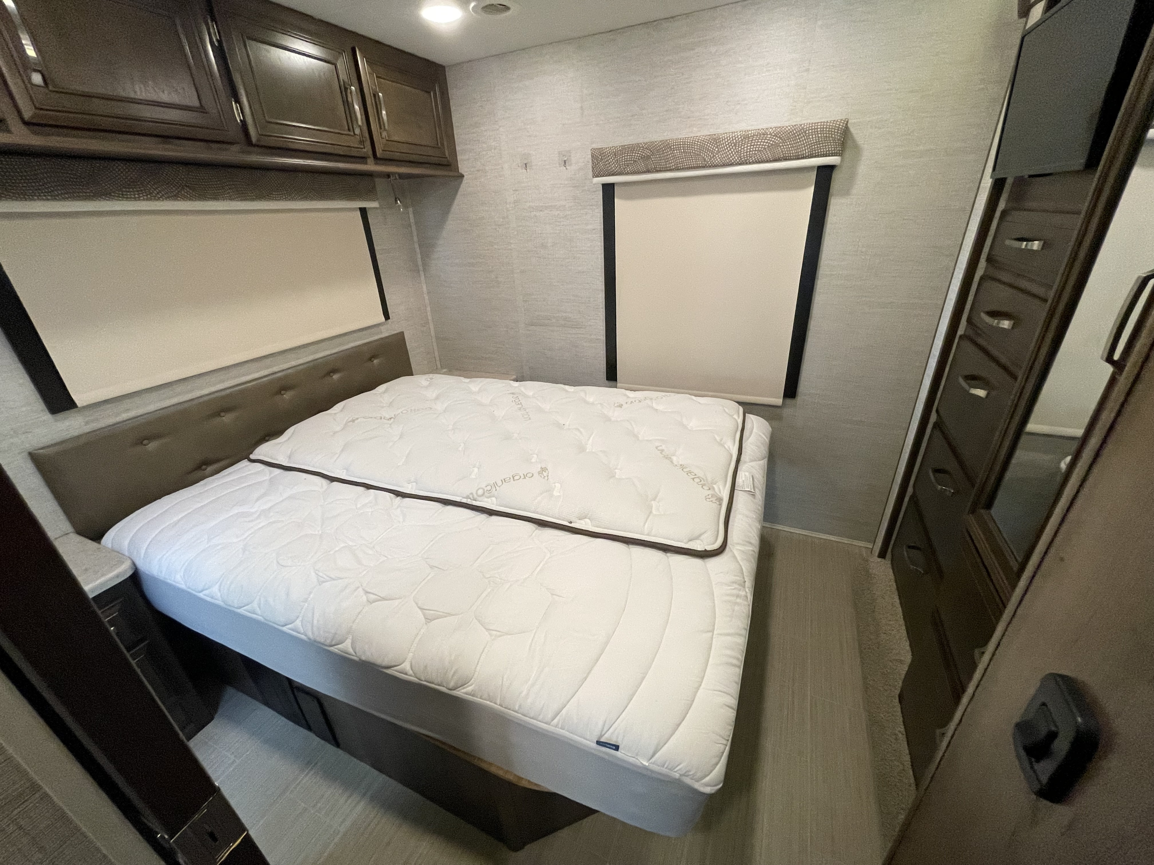 RV rental bedroom featuring a comfortable bed, upholstered headboard, overhead cabinets, and patterned valances.. Entegra Coach Esteem 2021