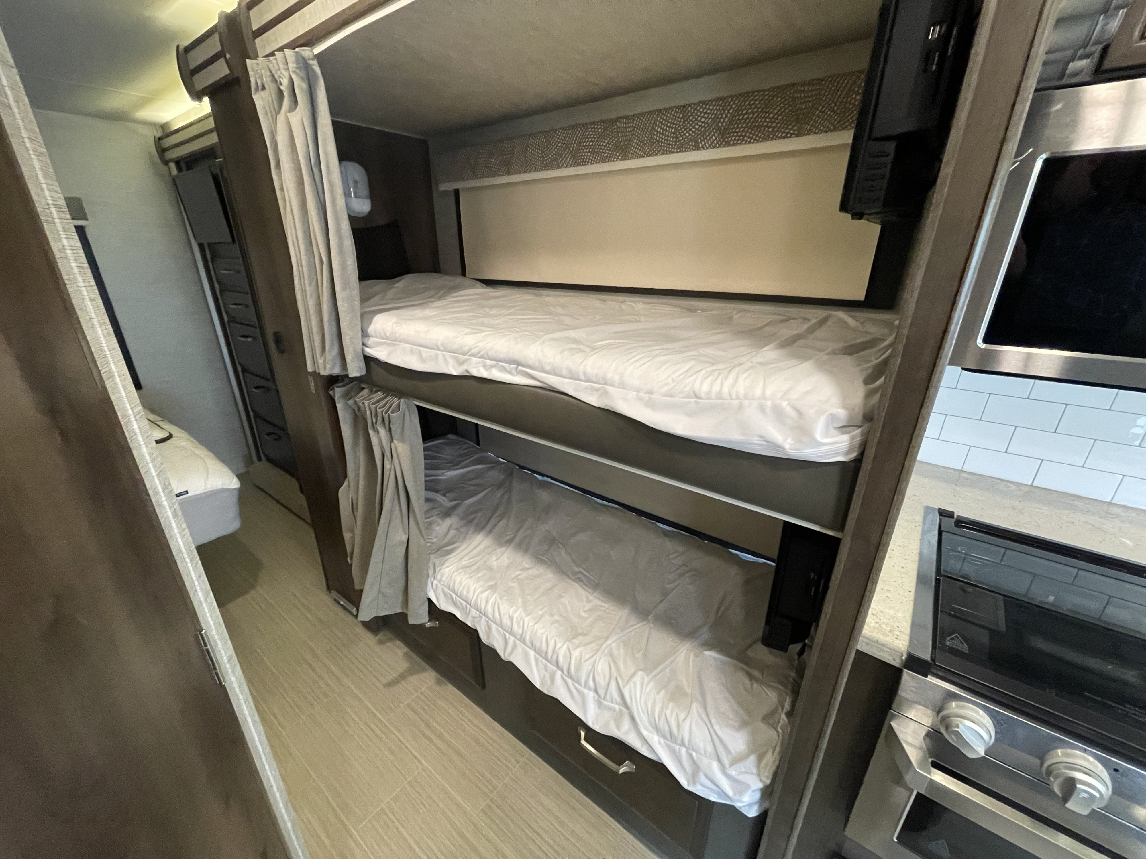 Cozy RV rental interior featuring comfortable bunk beds and a compact kitchen with a microwave and stove.. Entegra Coach Esteem 2021
