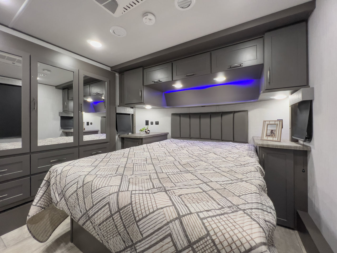 Modern gray RV rental bedroom with spacious storage, comfortable bed, mirrored wardrobe, and ambient lighting.. Grand Design Momentum 2023