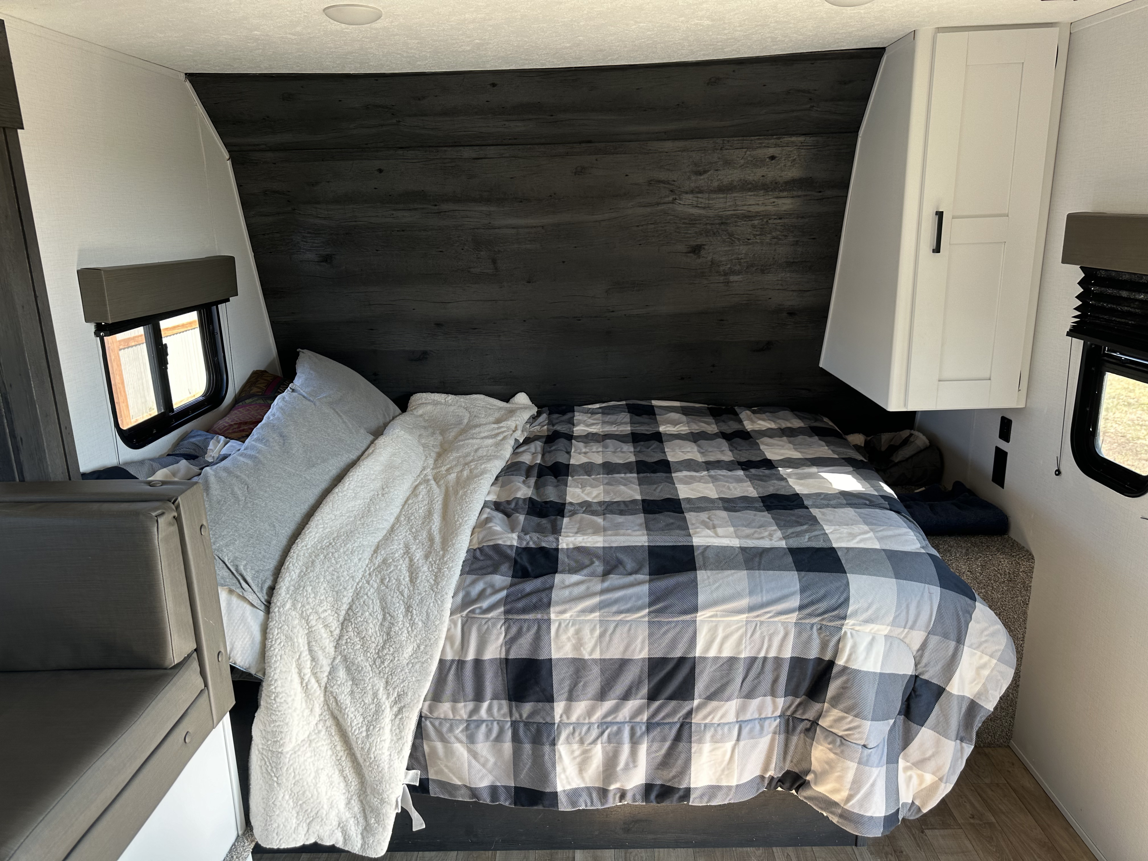 Cozy RV rental bedroom features a bed with plaid comforter, dark wood wall, white cabinet, and a small window.. Keystone RV Hideout 2021