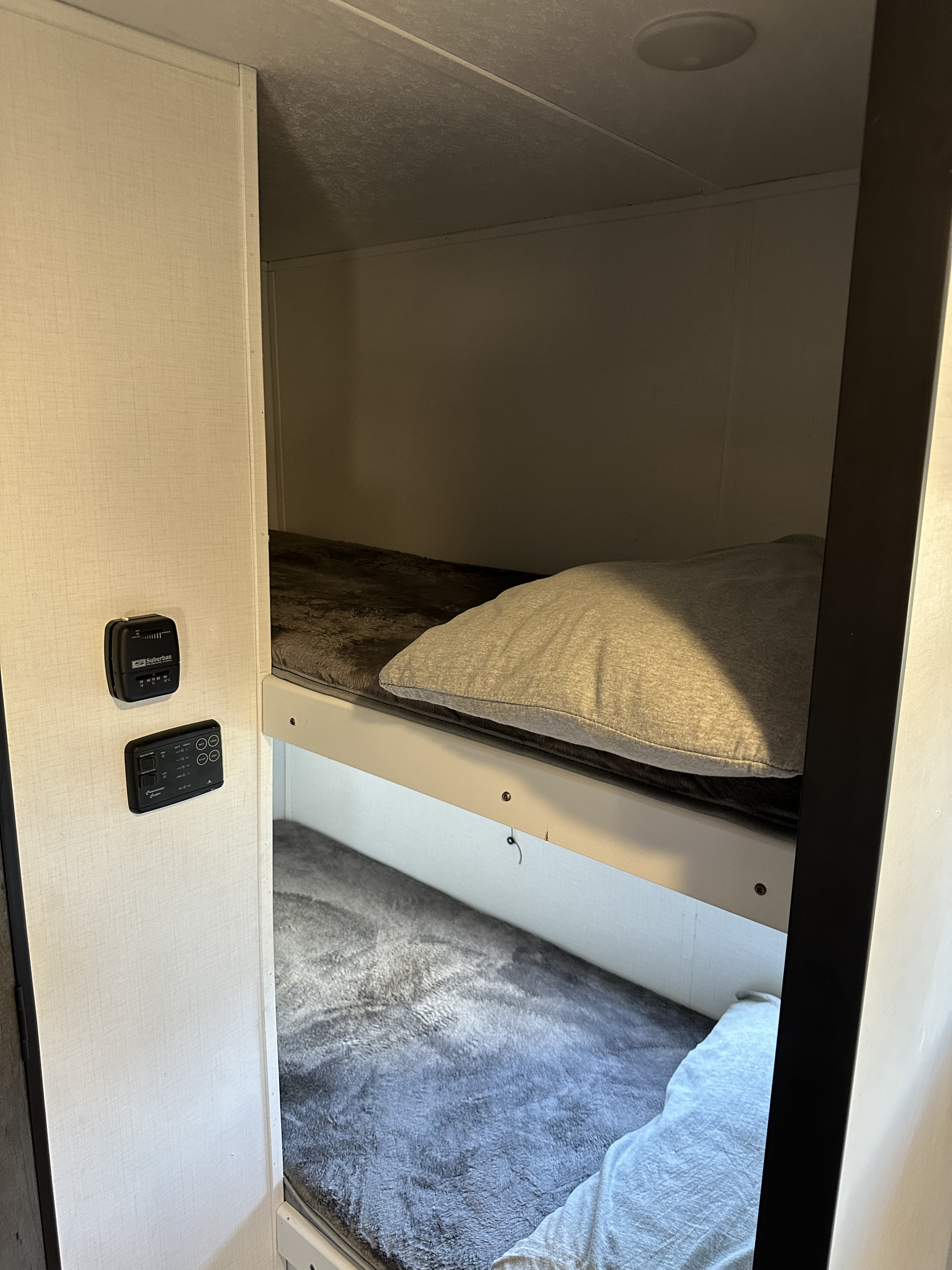 This RV rental image displays cozy bunk beds with plush blankets, and wall-mounted thermostat/utility controls.. Keystone RV Hideout 2021
