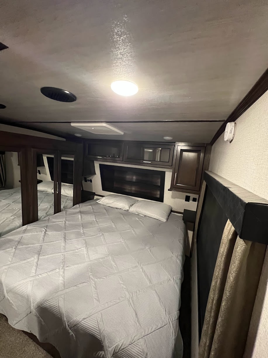 Inside an RV rental, this inviting bedroom features a spacious bed, built-in cabinets, and a mirrored wardrobe.. Dutchmen Voltage 2020