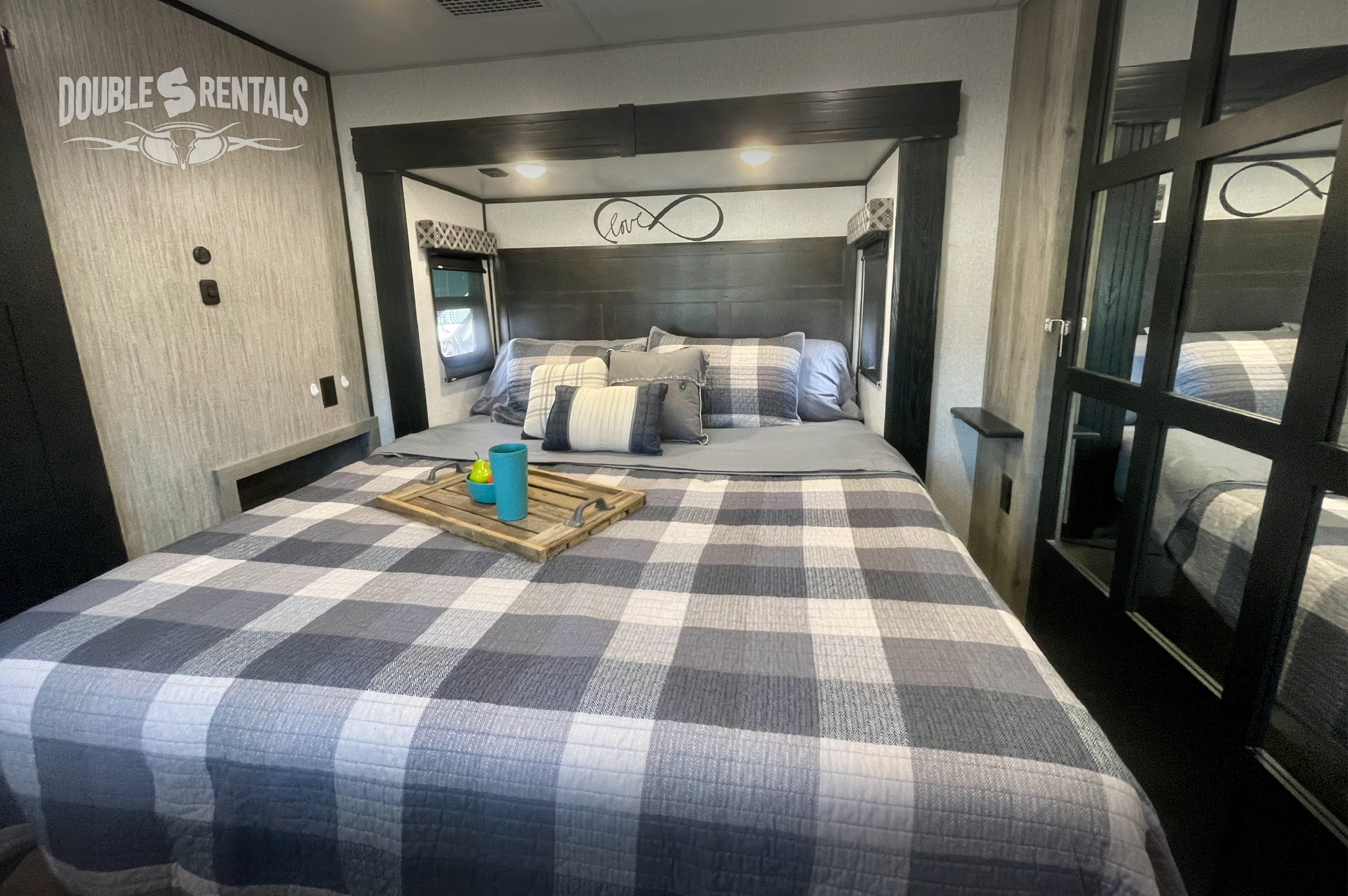 Cozy RV rental bedroom: large bed with grey plaid bedding, decorative pillows, and a wooden tray. Ideal for comfortable travel.. KZ Durango Gold 2022