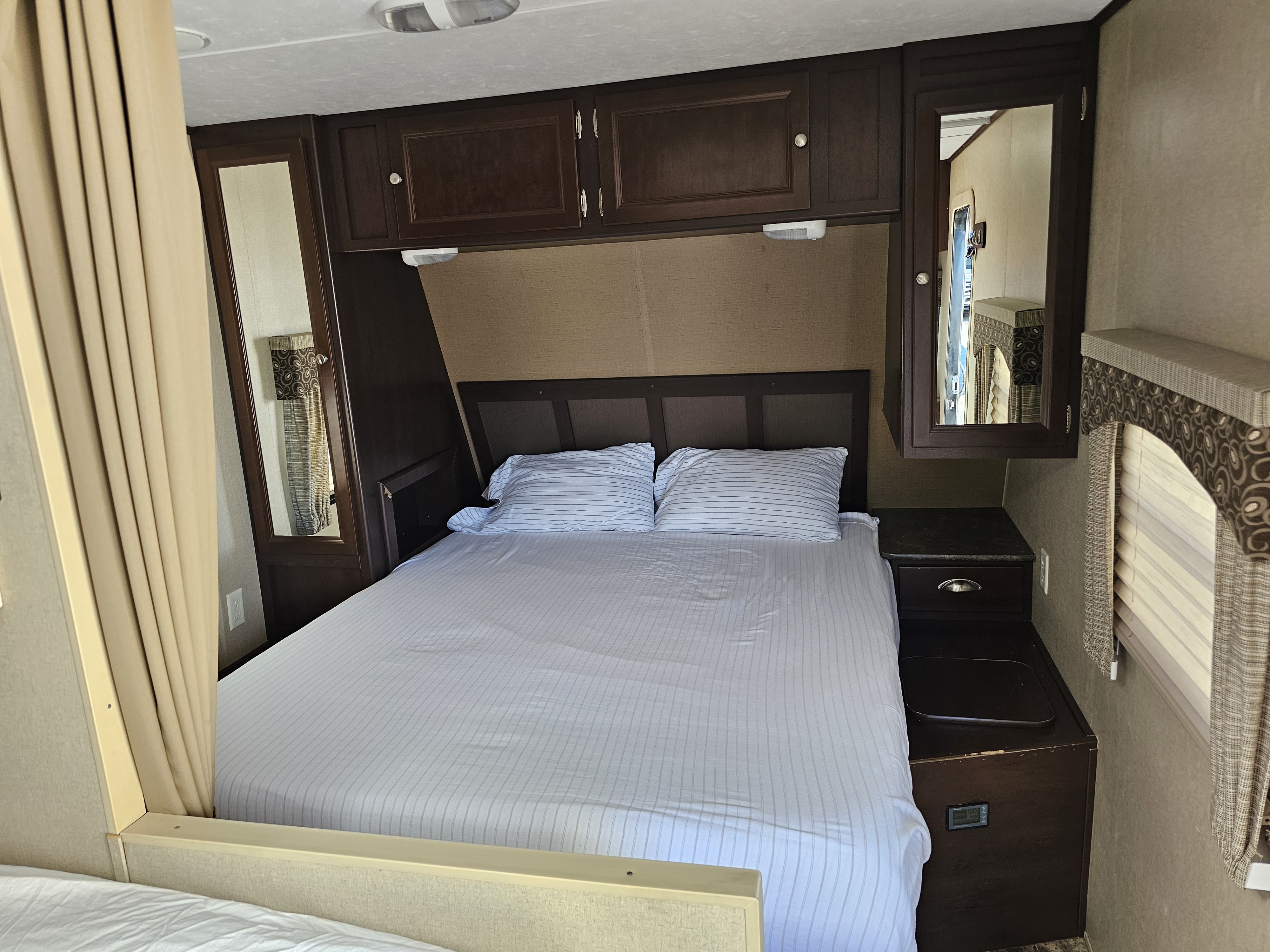Cozy RV rental bedroom featuring a queen bed with striped sheets, dark wood cabinets, mirrored storage, and a compact design.. Coleman Lantern 2014