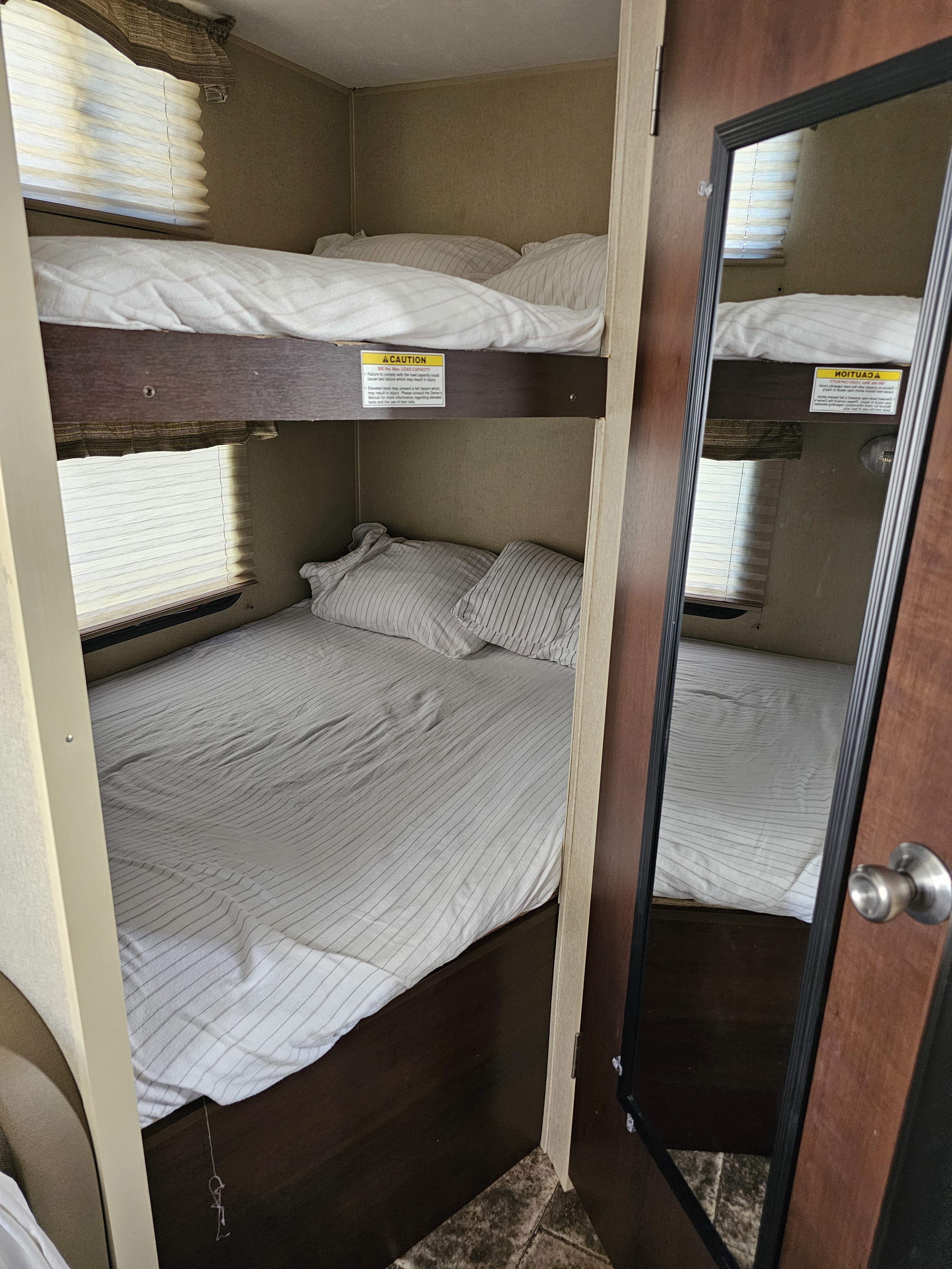 Inside an RV rental, compact bunk beds with striped bedding and a window create a cozy sleeping area.. Coleman Lantern 2014