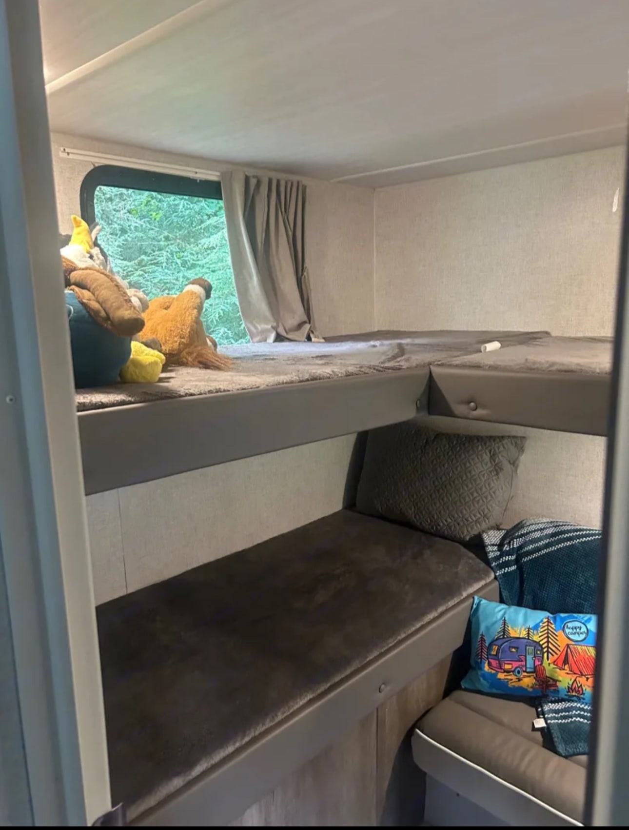 RV rental bunk beds: a cozy sleeping area. Plush toys on the top bunk, a window view of trees, and pillows on the lower bunk.. Forest River Salem Cruise Lite 2021