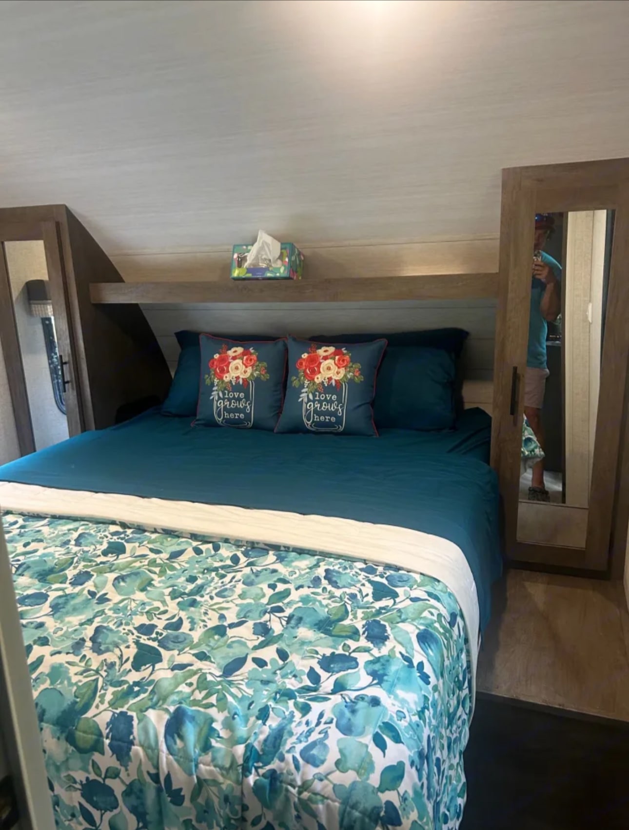 This cozy RV rental bedroom features a blue and floral bed with decorative pillows, a tissue box, and built-in storage.. Forest River Salem Cruise Lite 2021