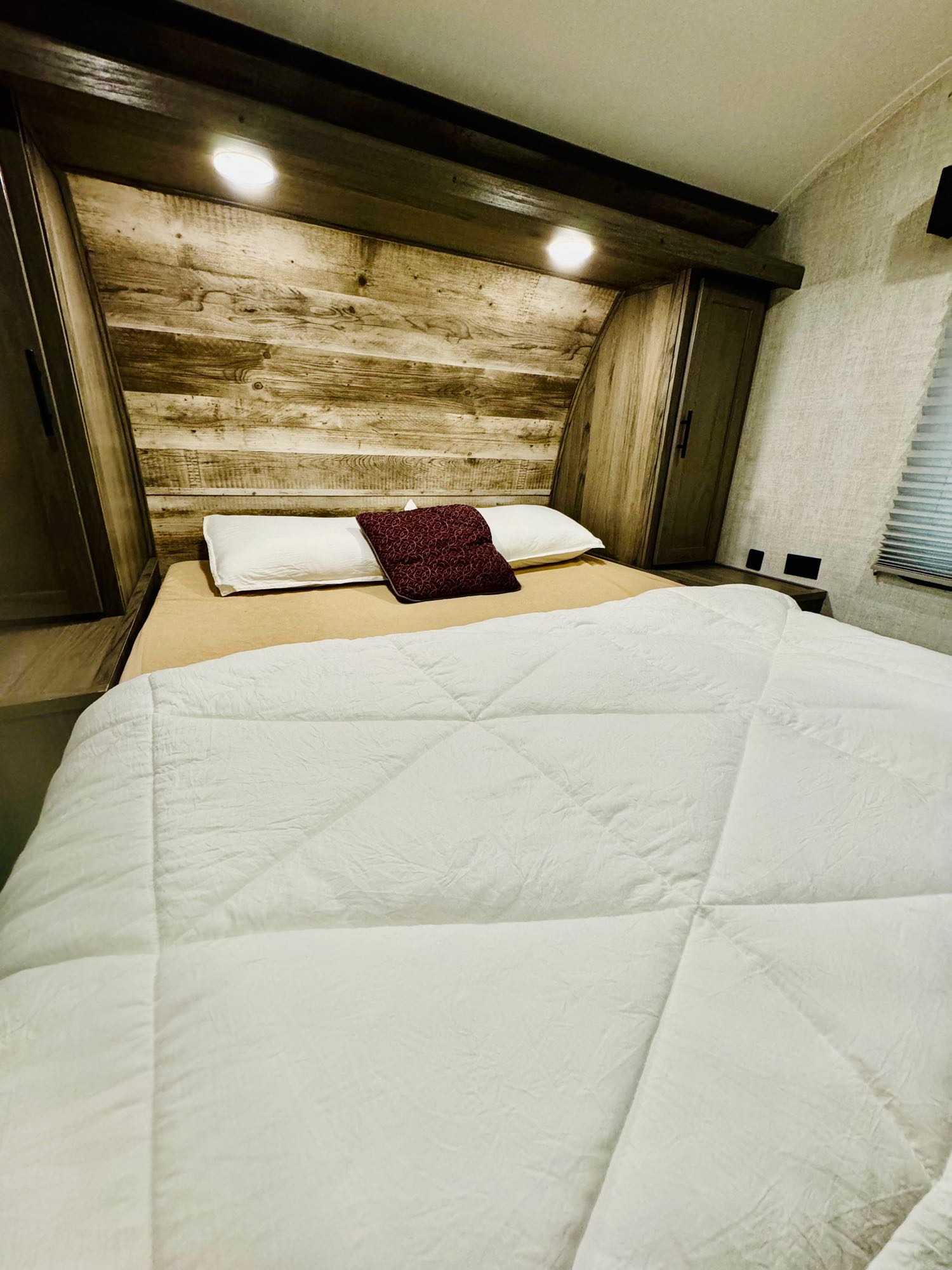 Inside an RV rental: a compact bedroom with a white bed, rustic wood headboard, built-in cabinets, and warm lighting.. Gulf Stream Ameri-Lite 2021