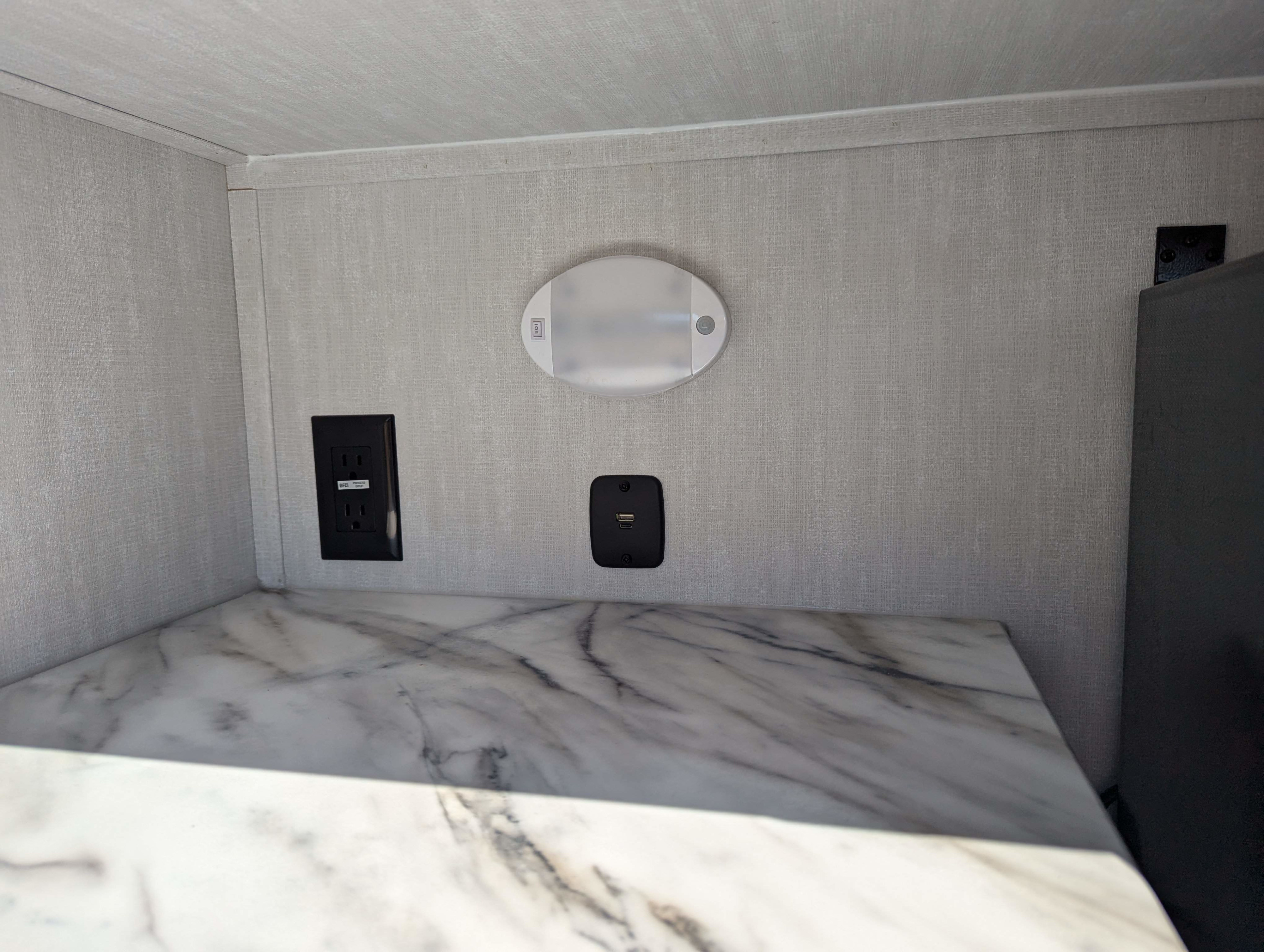 Modern RV rental interior with power outlets, USB ports, and LED light above a marble-look countertop, offering convenience.. Coachmen Apex Nano 2024