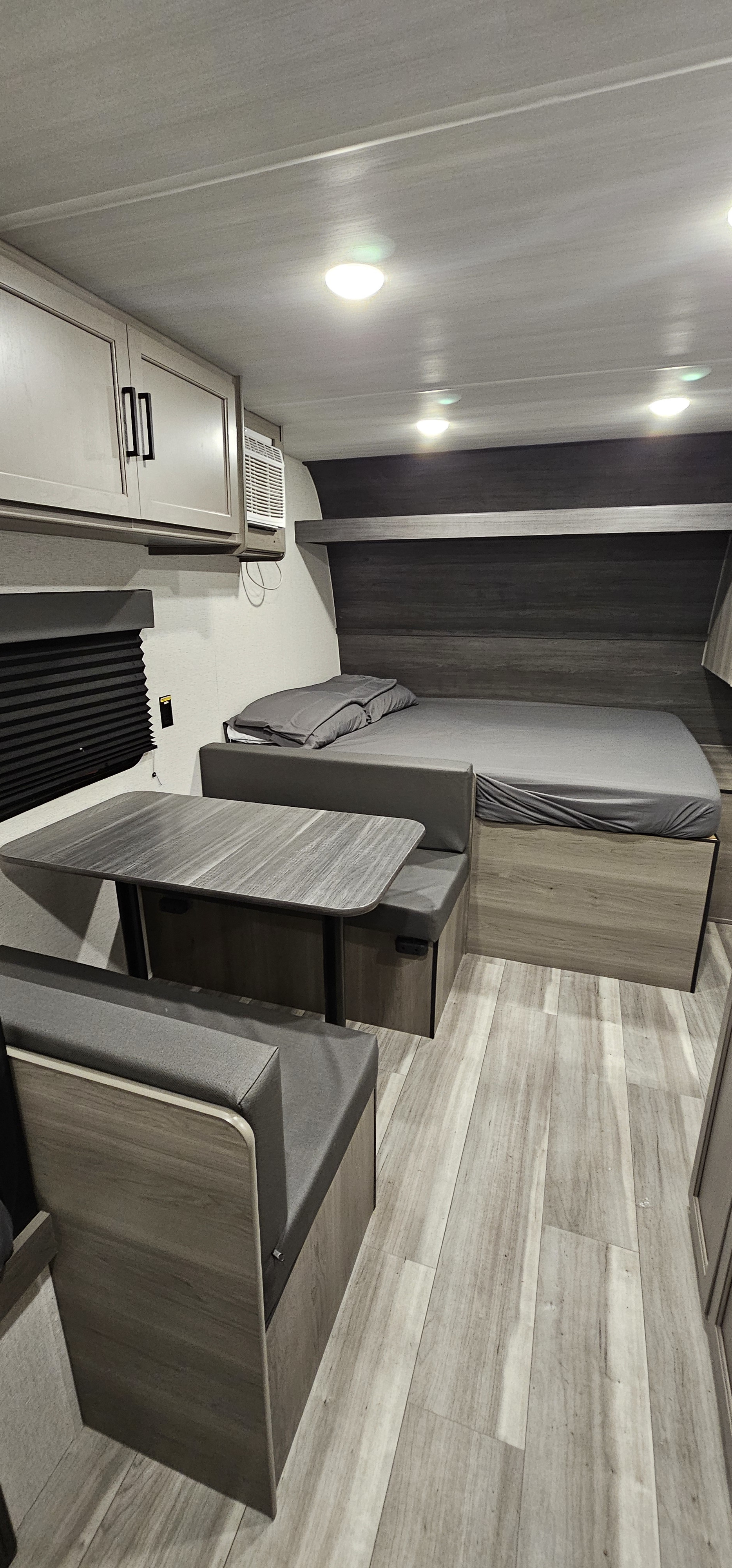 RV rental interior featuring a modern design with bed, dinette, overhead cabinets, and light wood flooring.. Keystone RV Hideout Sport 2024