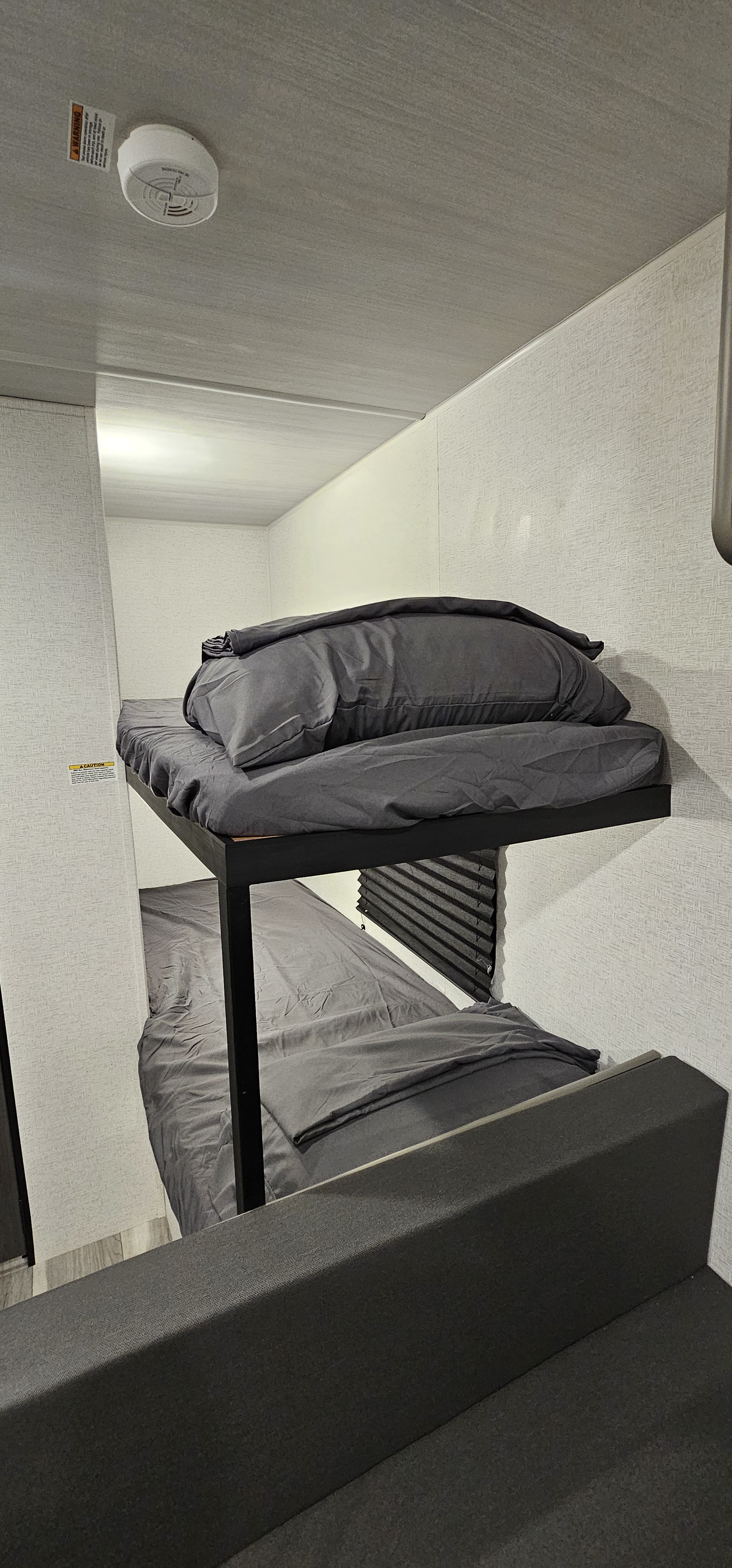 RV rental bunk beds with gray bedding, a smoke detector on the ceiling, and a seating area in a compact interior.. Keystone RV Hideout Sport 2024
