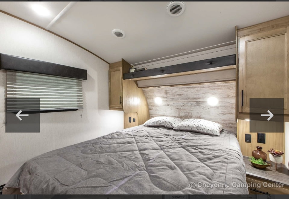 RV rental bedroom with a large bed, overhead cabinets, window, and modern lighting for a cozy stay.. Forest River Cherokee Arctic Wolf 2023