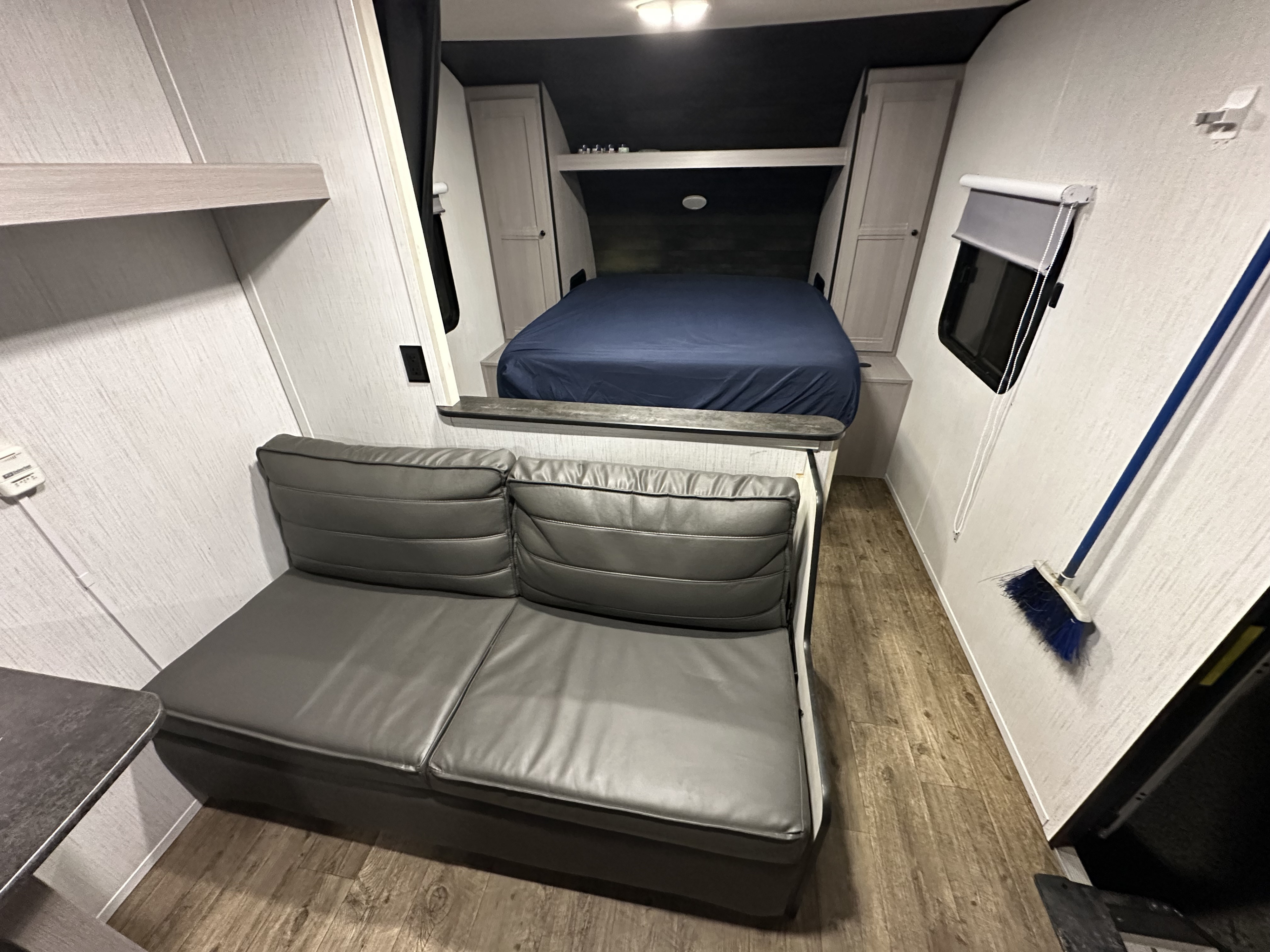Inside this RV rental: a cozy gray sofa, elevated bed, and compact living space with wood-look flooring.. Heartland RVs Trail Runner 2022