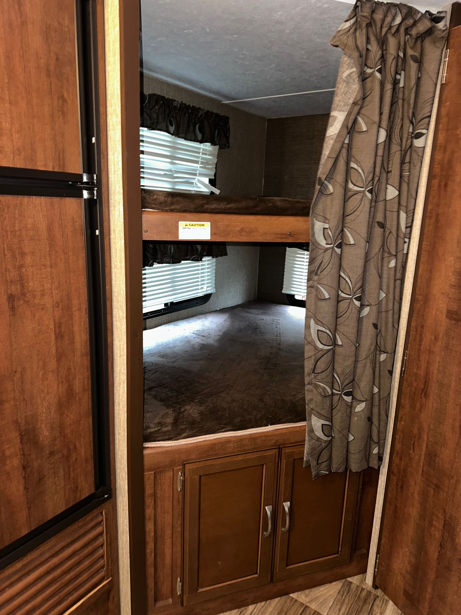 This RV rental shows the interior's double bunk beds, complete with blinds, patterned curtains, and wooden cabinetry.. Keystone RV Passport Grand Touring 2016
