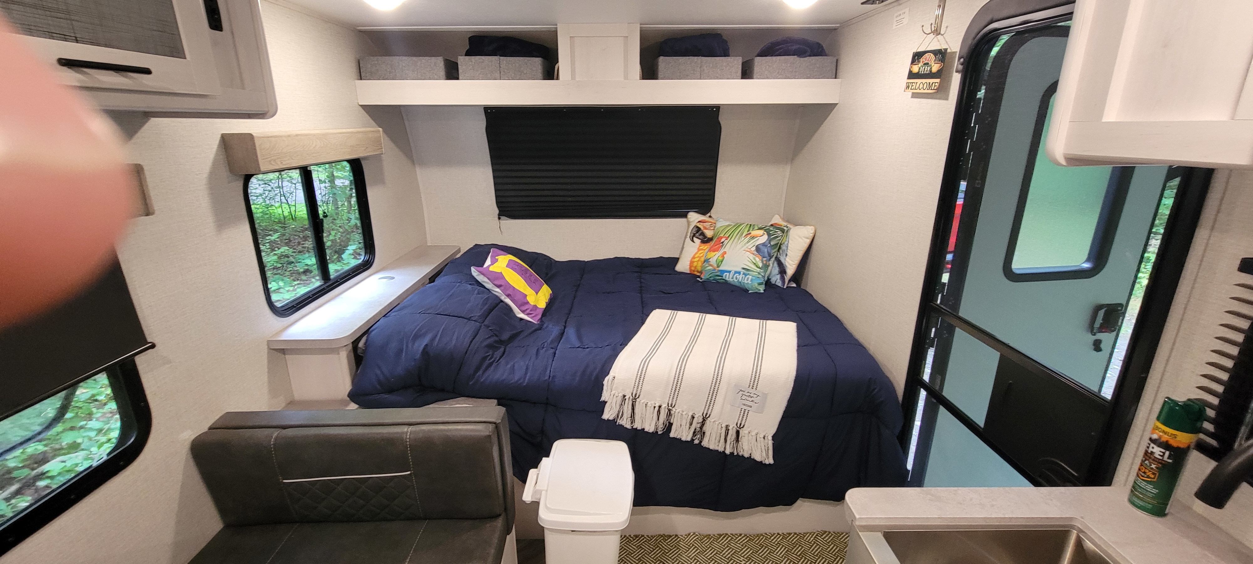 Cozy RV rental interior: A compact bedroom featuring a navy bed, pillows, windows with nature views, and overhead storage.. Dutchmen Coleman Rubicon 2021