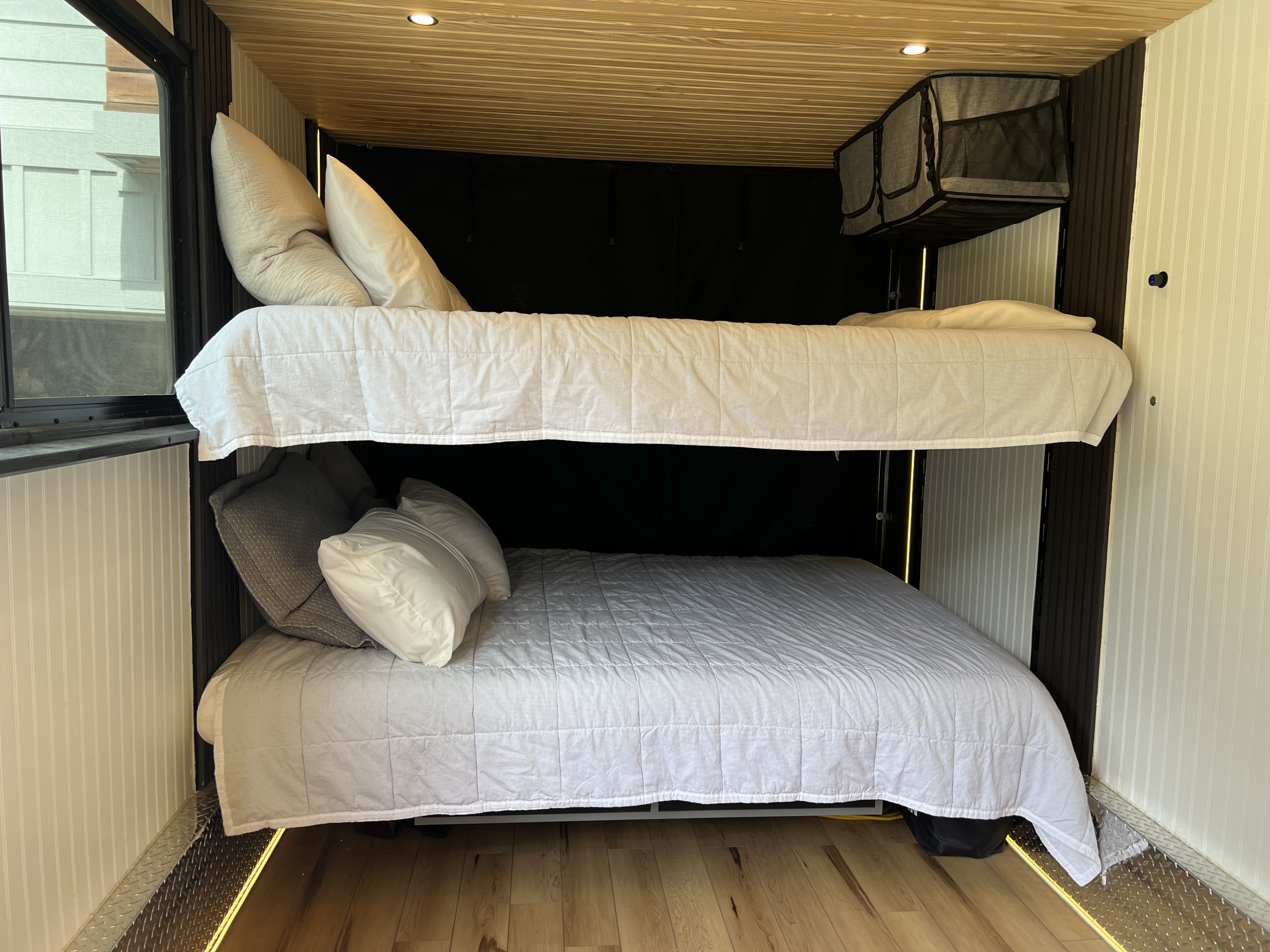 An RV rental's cozy interior features stacked bunk beds, neatly made with white and grey bedding, and a light wood ceiling.. Custom Camper 2024