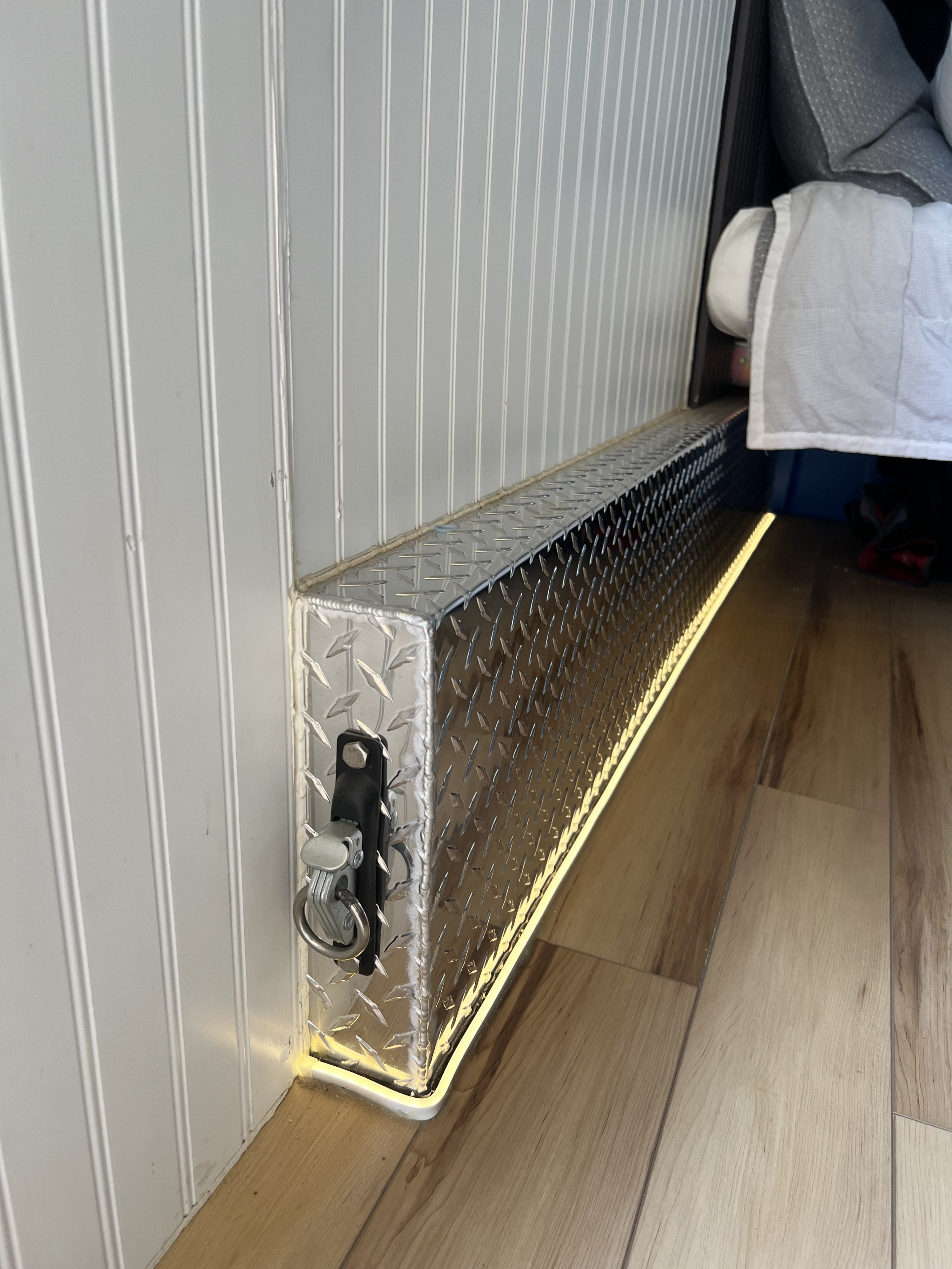 RV rental interior features a diamond plate storage box with a latch, under-mount accent lighting, and wood-look flooring.. Custom Camper 2024