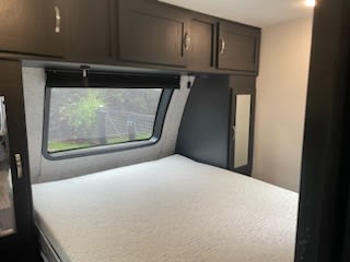 RV rental bedroom: a comfy bed under a large window, flanked by dark cabinets and storage. Perfect for travel!. Coachmen 257 BHS 2021