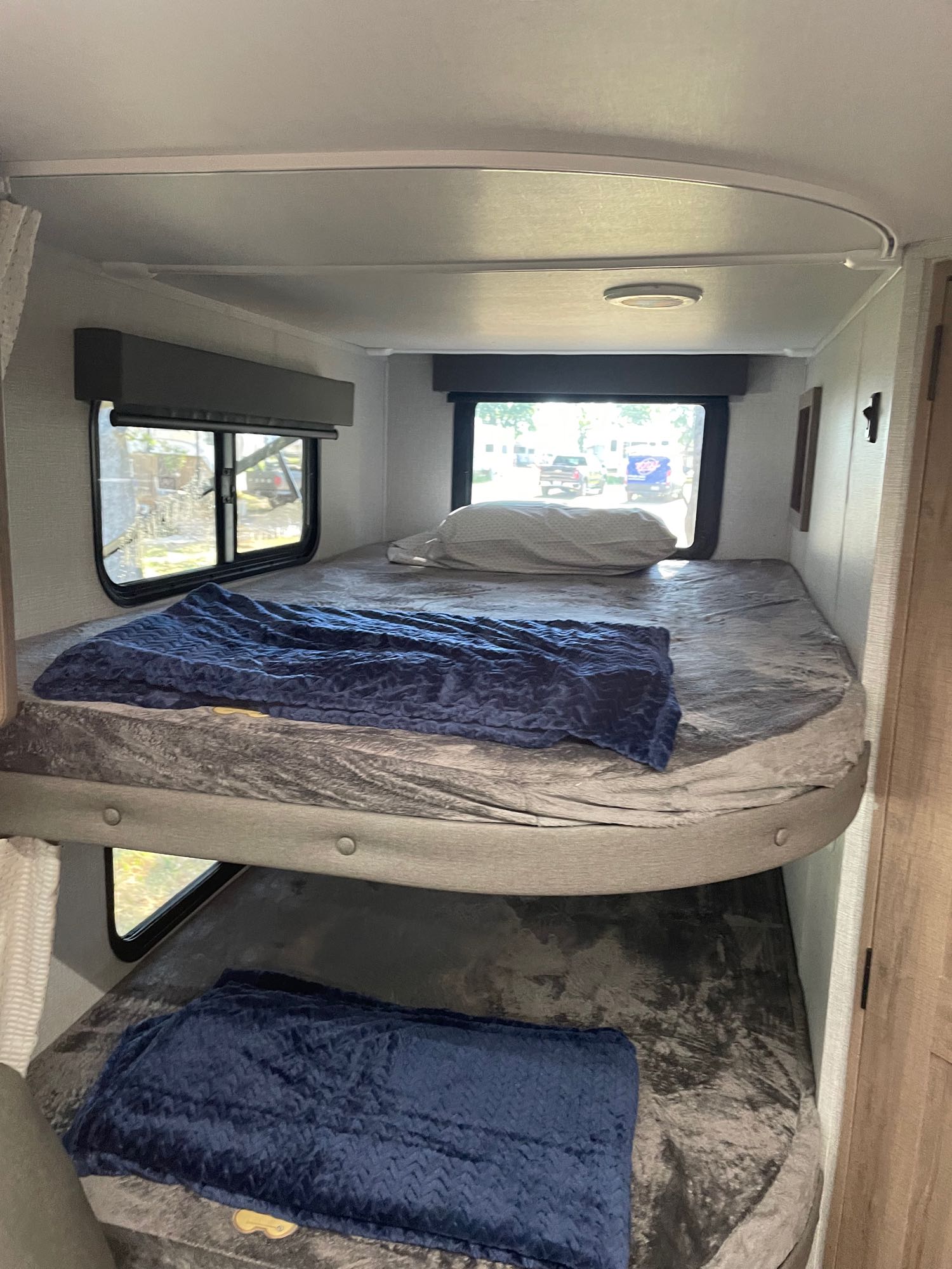 Two cozy bunk beds in an RV rental, each with a grey sheet and blue blanket, offering a comfortable sleeping area.. Grand Design Imagine XLS 2024