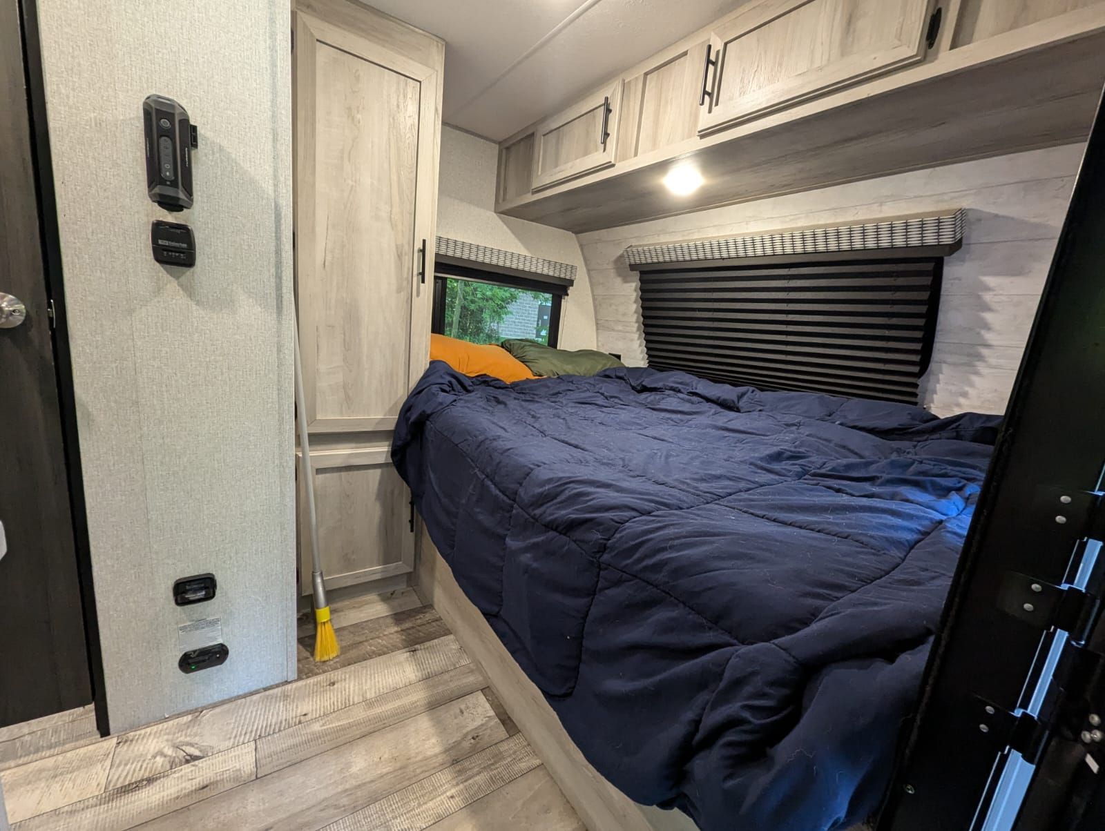 View inside an RV rental bedroom: a large bed with blue comforter, overhead cabinets, windows, and light wood flooring.. KZ Escape Hatch 2022