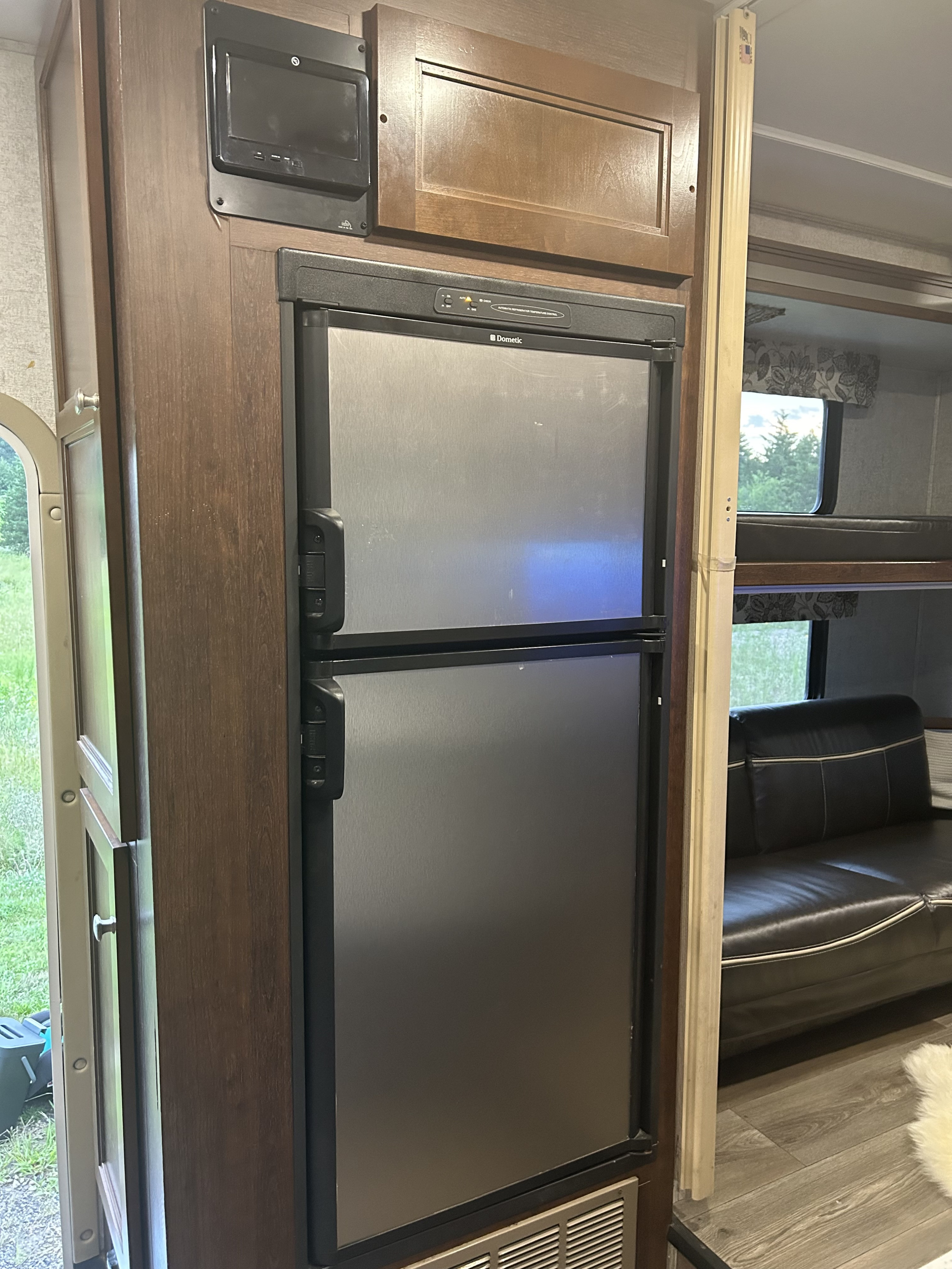 RV rental interior: a Dometic refrigerator, adjacent to a door revealing outdoor views, with a bunk bed and couch visible in the rear.. Forester Forester Motorhome 2017
