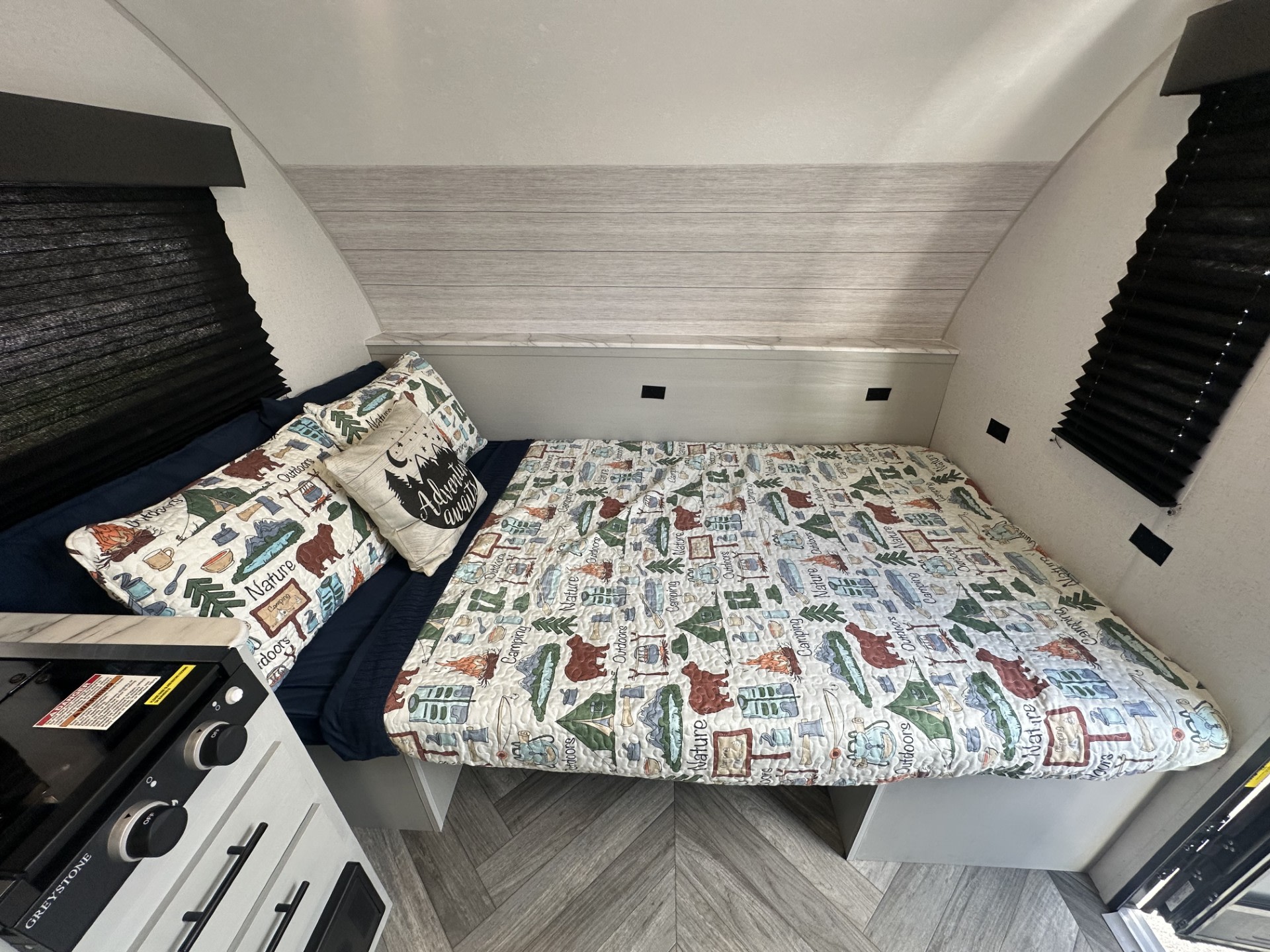 Cozy RV rental bedroom with camping-themed bedding and integrated kitchen counter. Perfect for adventure travel.. Forest River Wildwood 2022